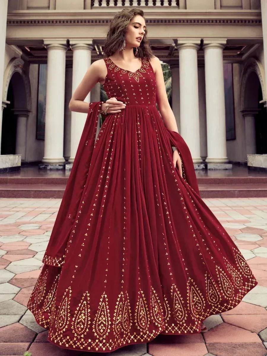 Woman in maroon ethnic gown with gold embroidery, sleeveless, standing outdoors