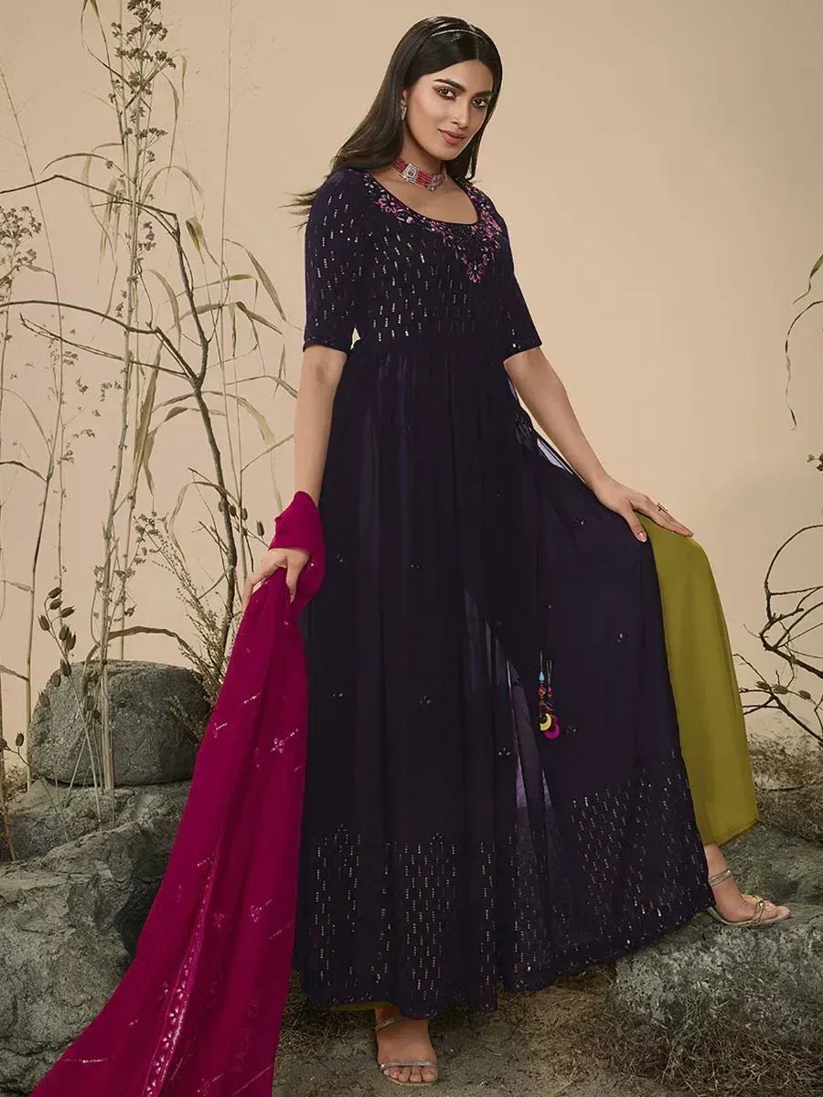 Woman in a navy blue ethnic gown with pink embroidery and magenta dupatta, standing outdoors.