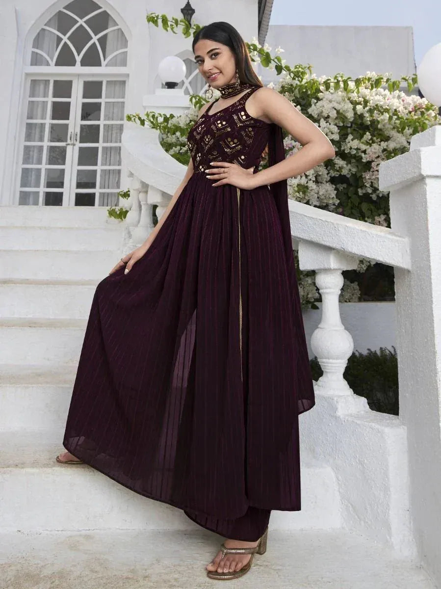 Woman in maroon embroidered ethnic gown posing on white staircase outdoors