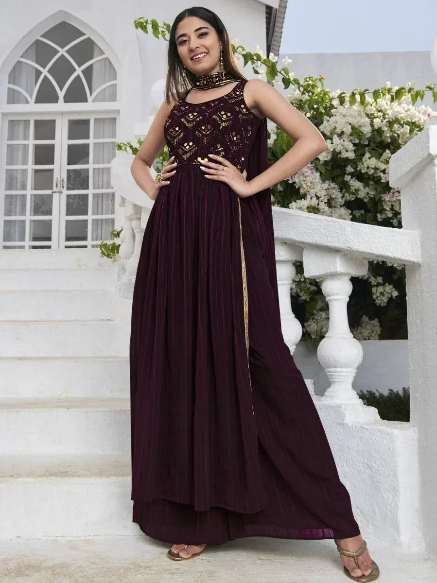 Woman in maroon ethnic gown with gold embroidery standing on white steps outdoors