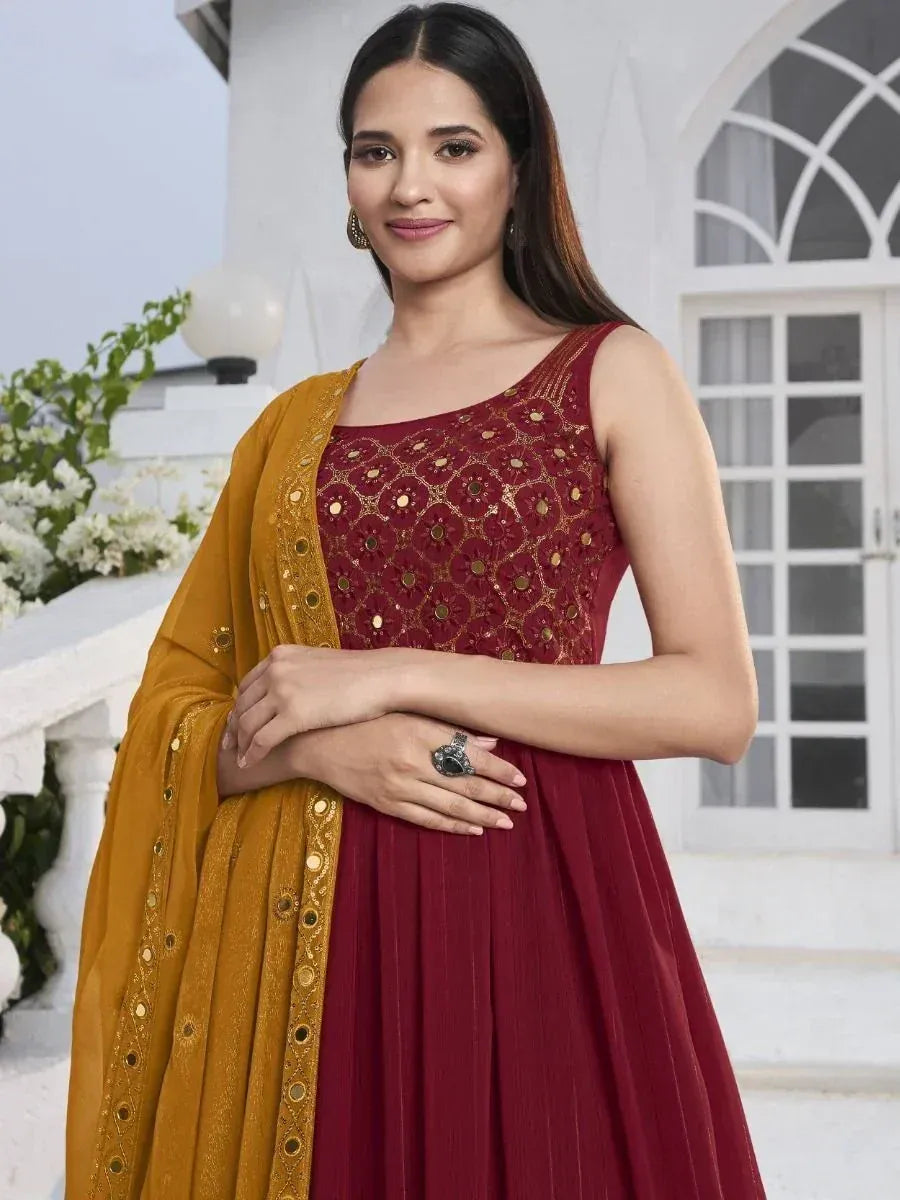 Woman in maroon embroidered ethnic gown with mustard dupatta, standing outdoors