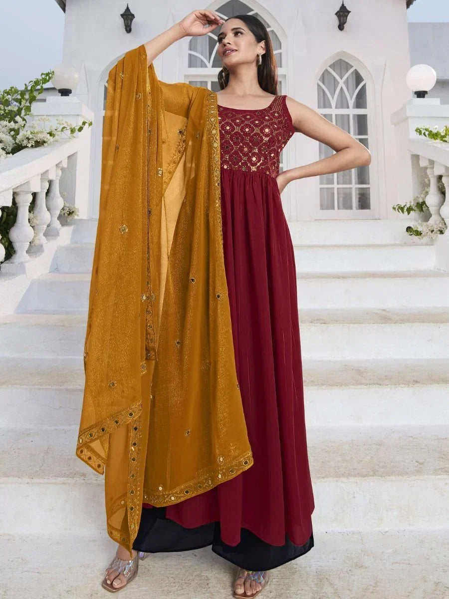 Woman in maroon ethnic gown with gold embroidery and mustard dupatta on white stairs