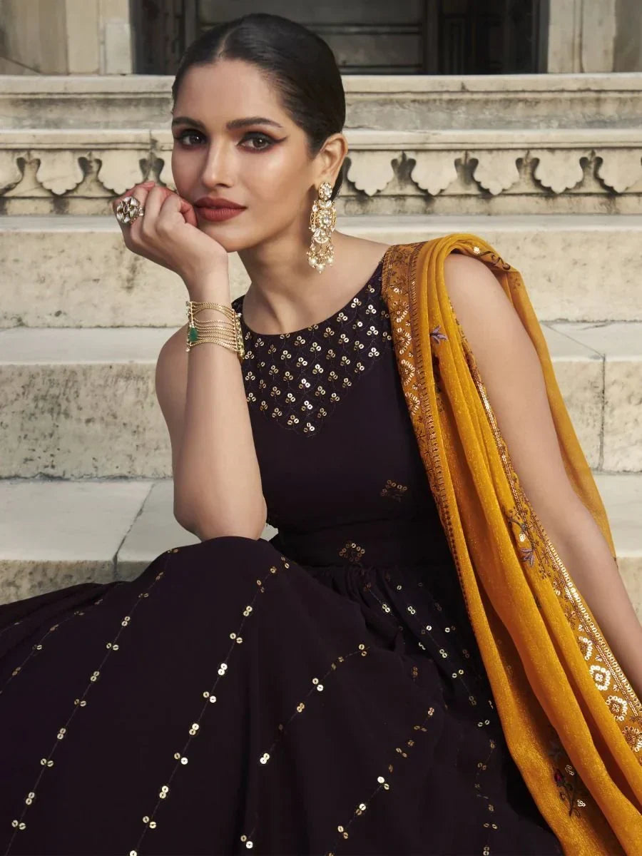 Woman in black designer lehenga with gold embroidery and mustard dupatta, ethnic jewelry