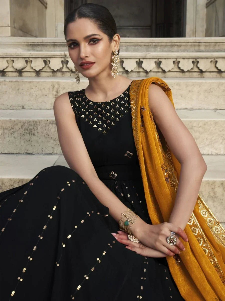 Woman in black designer lehenga with gold embellishments and mustard dupatta, ethnic jewelry