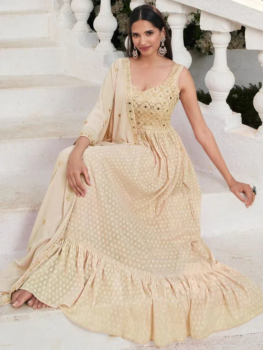 Woman in beige embroidered ethnic gown with dupatta, sitting on white steps