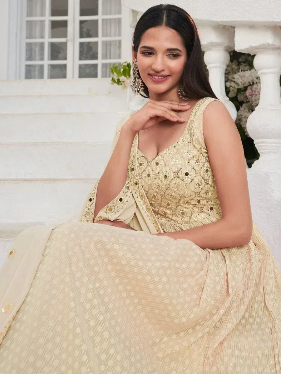 Woman in gold embroidered lehenga choli, sleeveless blouse, sitting on white stairs