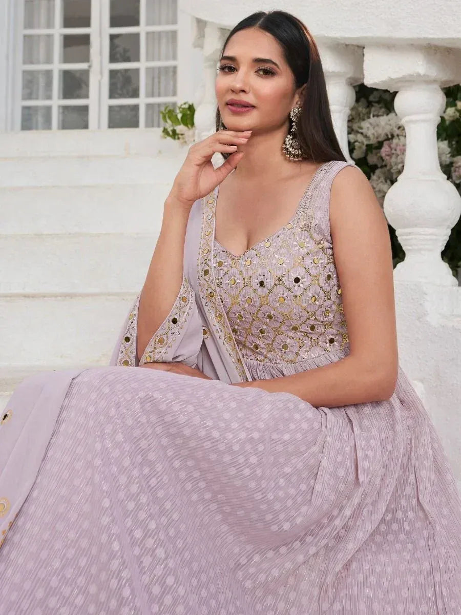 Woman in lilac embroidered ethnic gown with dupatta, sitting on white stairs