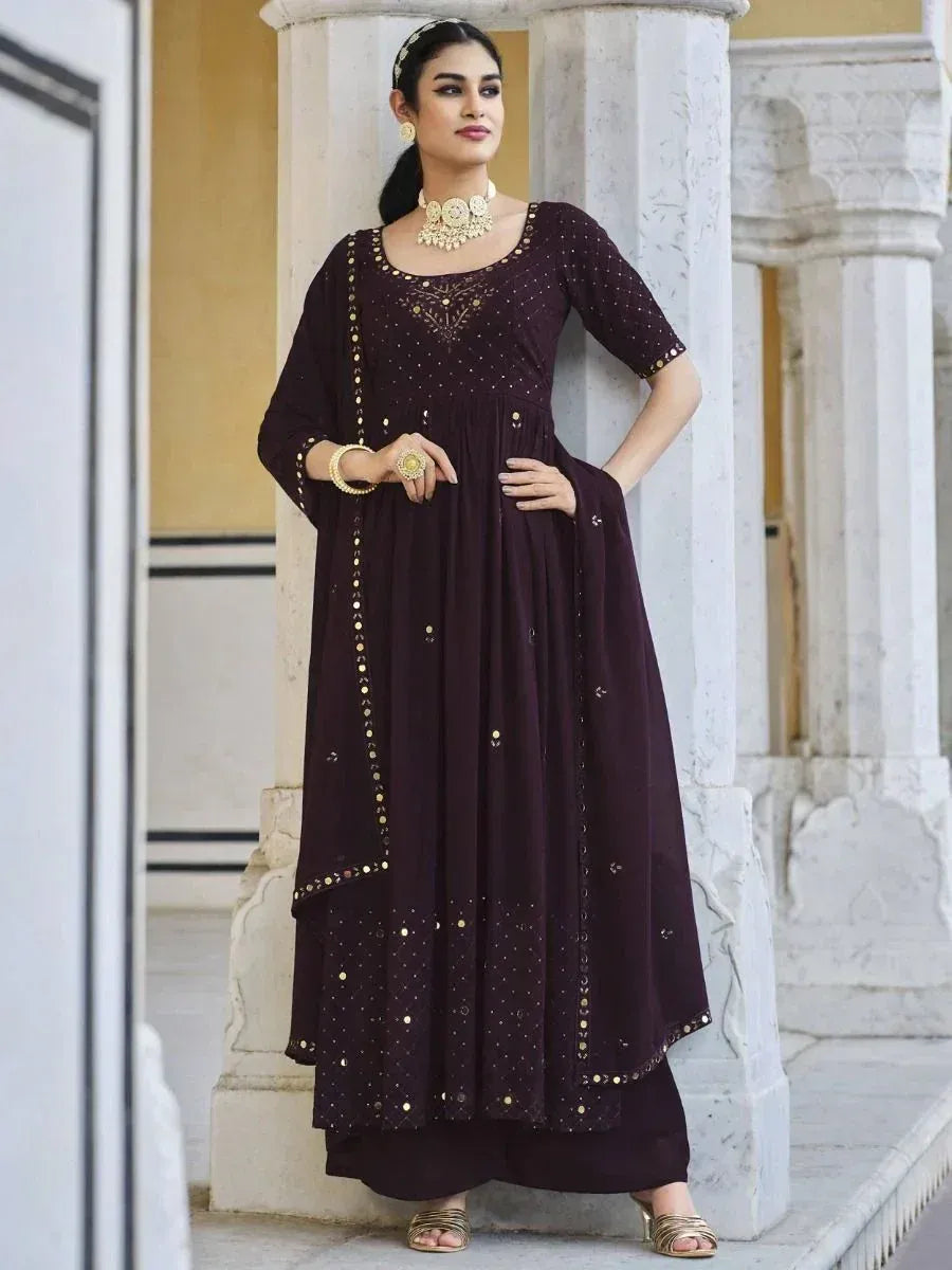 Woman wearing a maroon Indian ethnic gown with gold detailing, dupatta, and traditional jewelry.