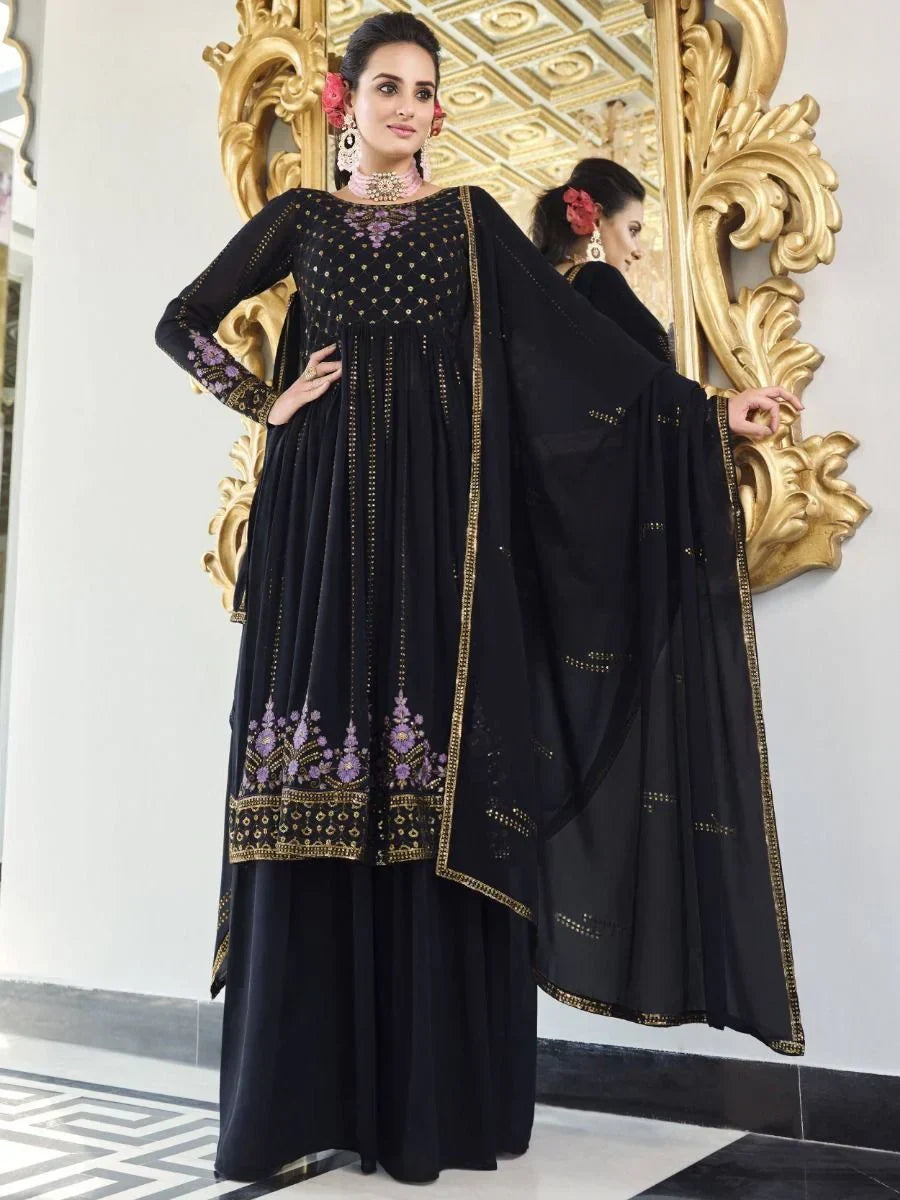 Woman in black embroidered Anarkali suit with gold and purple detailing, standing indoors