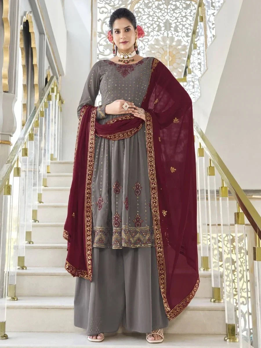 Woman in grey and maroon embroidered salwar kameez with dupatta on staircase