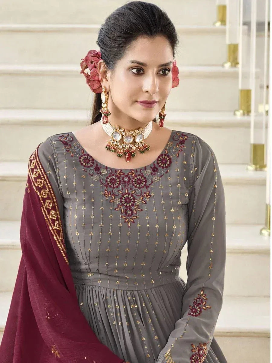 Woman in grey embroidered salwar kameez with maroon dupatta, floral jewelry, and updo hairstyle