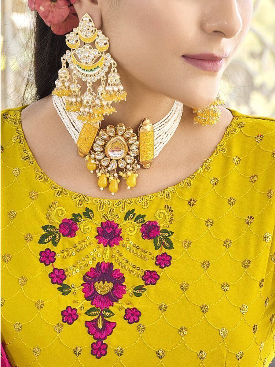 Yellow embroidered ethnic blouse with pink floral design, paired with gold jhumka earrings and pearl necklace