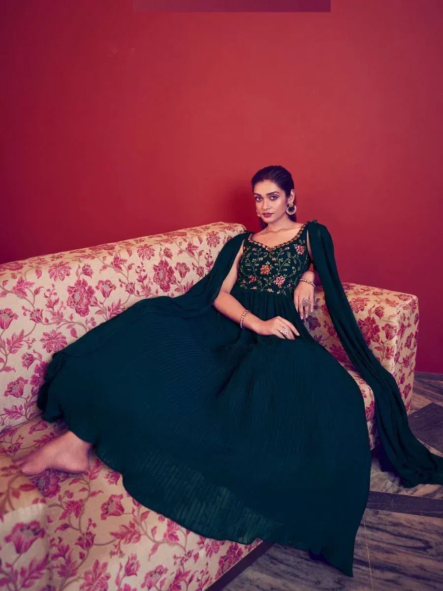Elegant green embroidered ethnic gown with floral detailing, styled on a floral sofa against a red backdrop.