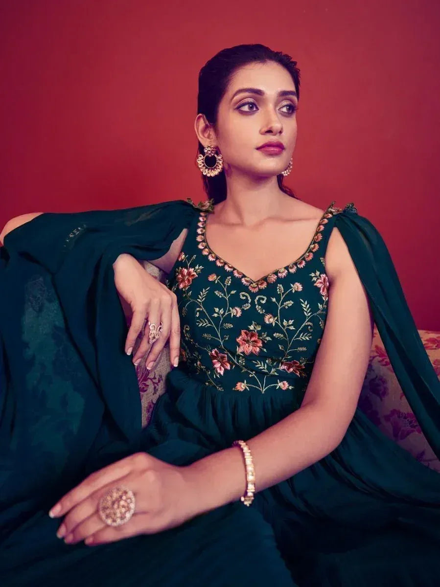 Woman in green floral embroidered ethnic gown with matching dupatta, elegant jewelry, red backdrop