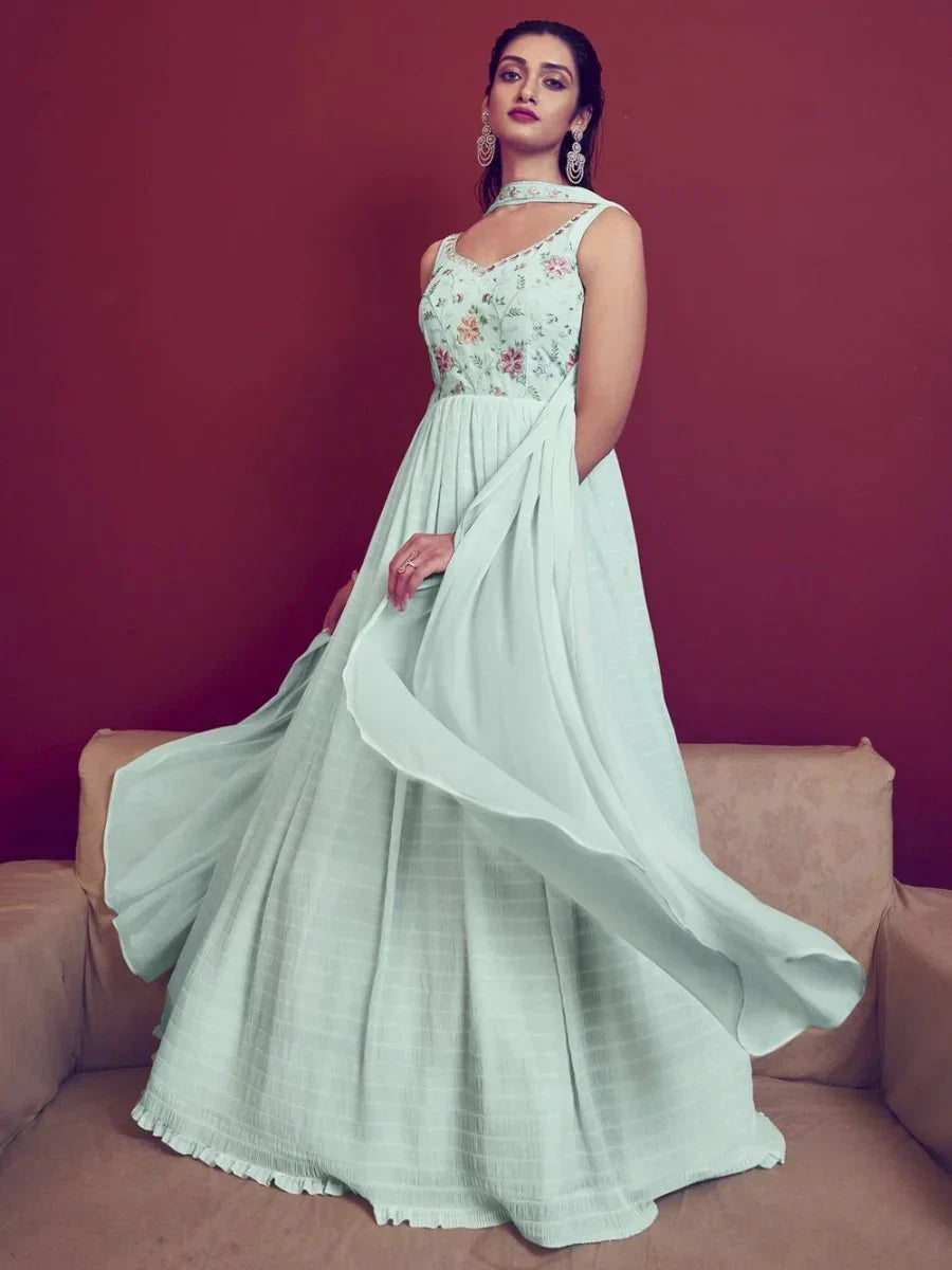 Woman in pastel green ethnic gown with floral embroidery and sheer dupatta, indoors