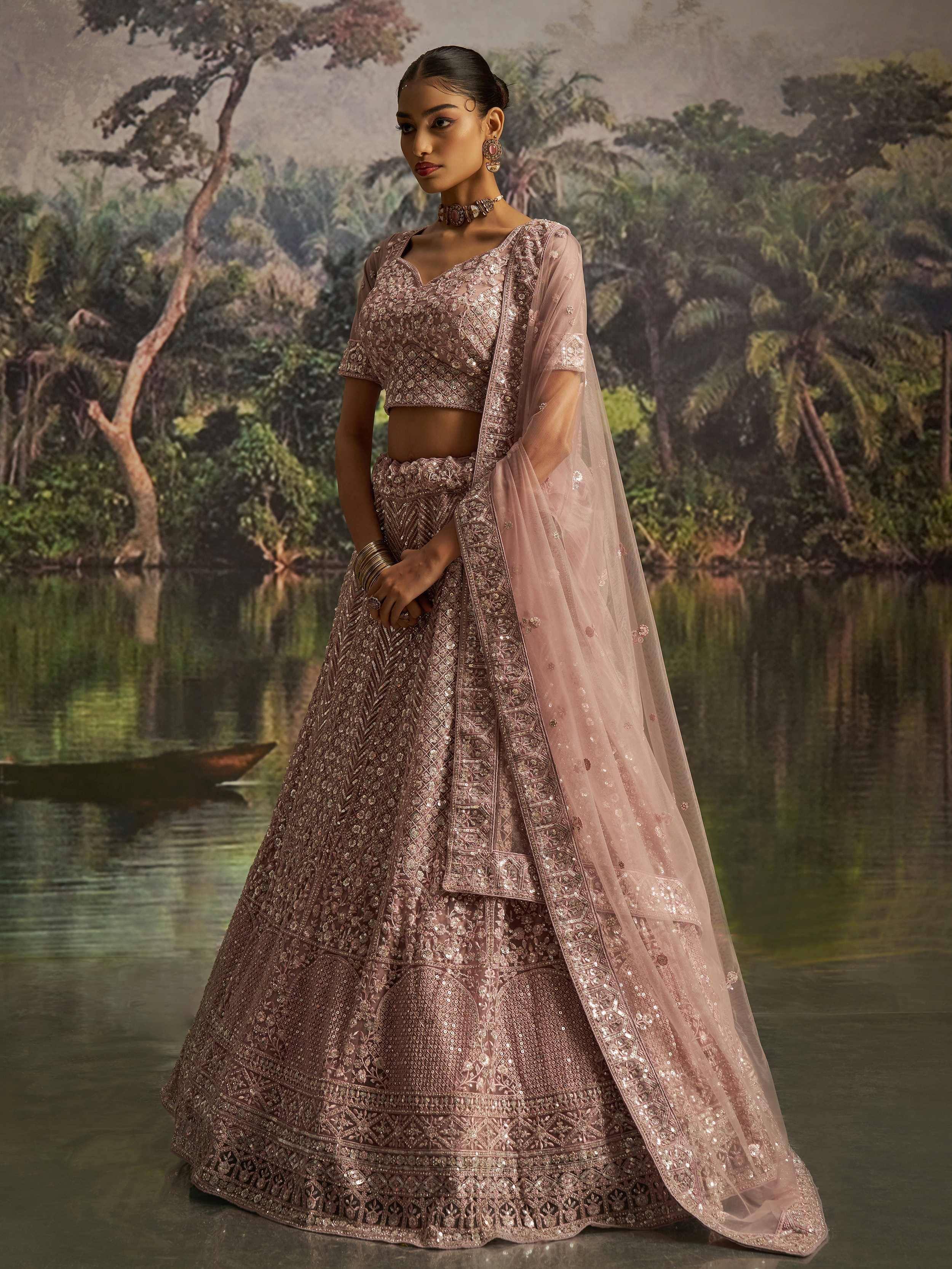 Elegant dusty pink designer lehenga choli with intricate embroidery and sheer dupatta, perfect for weddings.