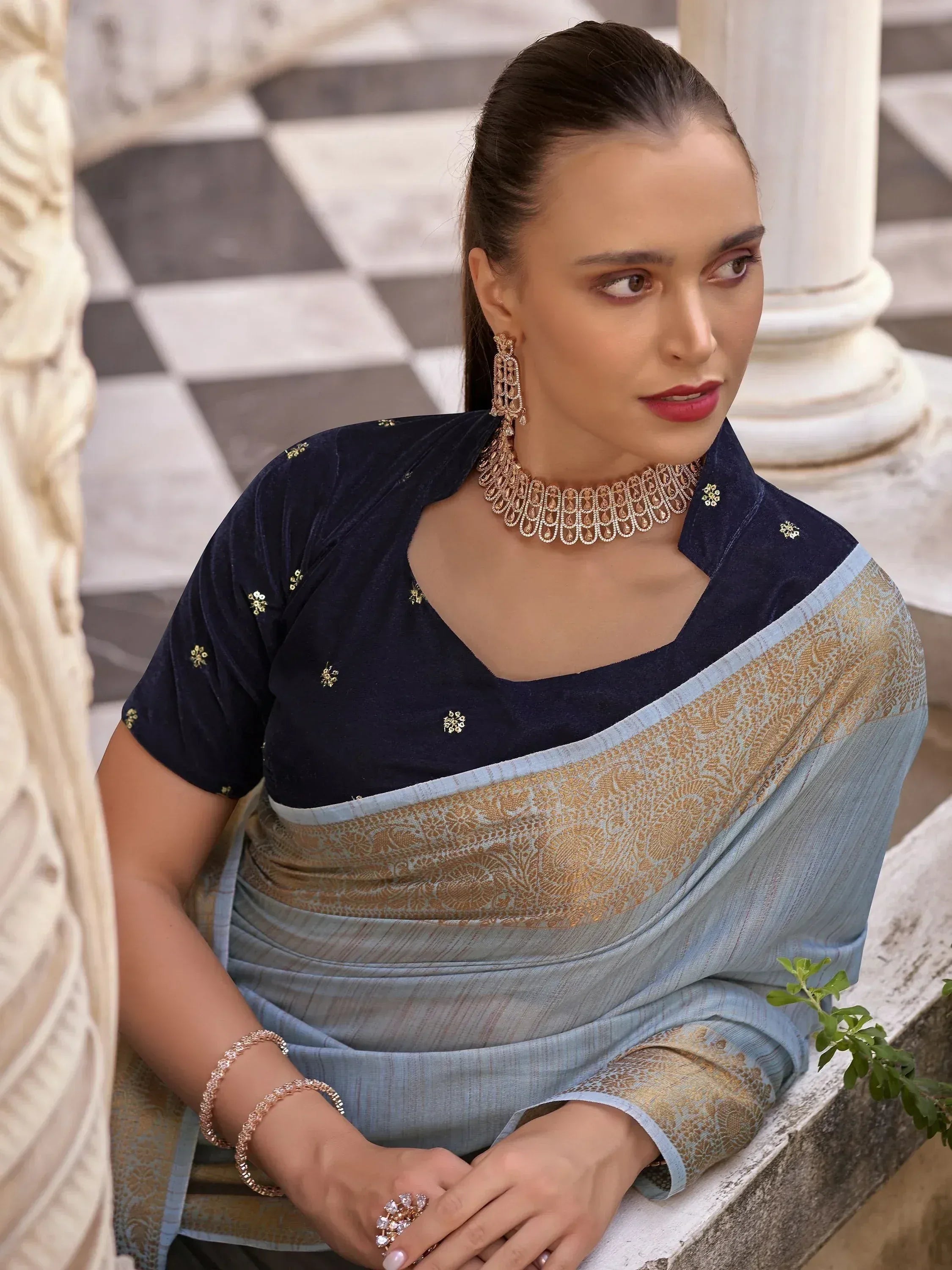 Woman in elegant blue saree with gold embroidery and velvet blouse, styled with traditional jewelry