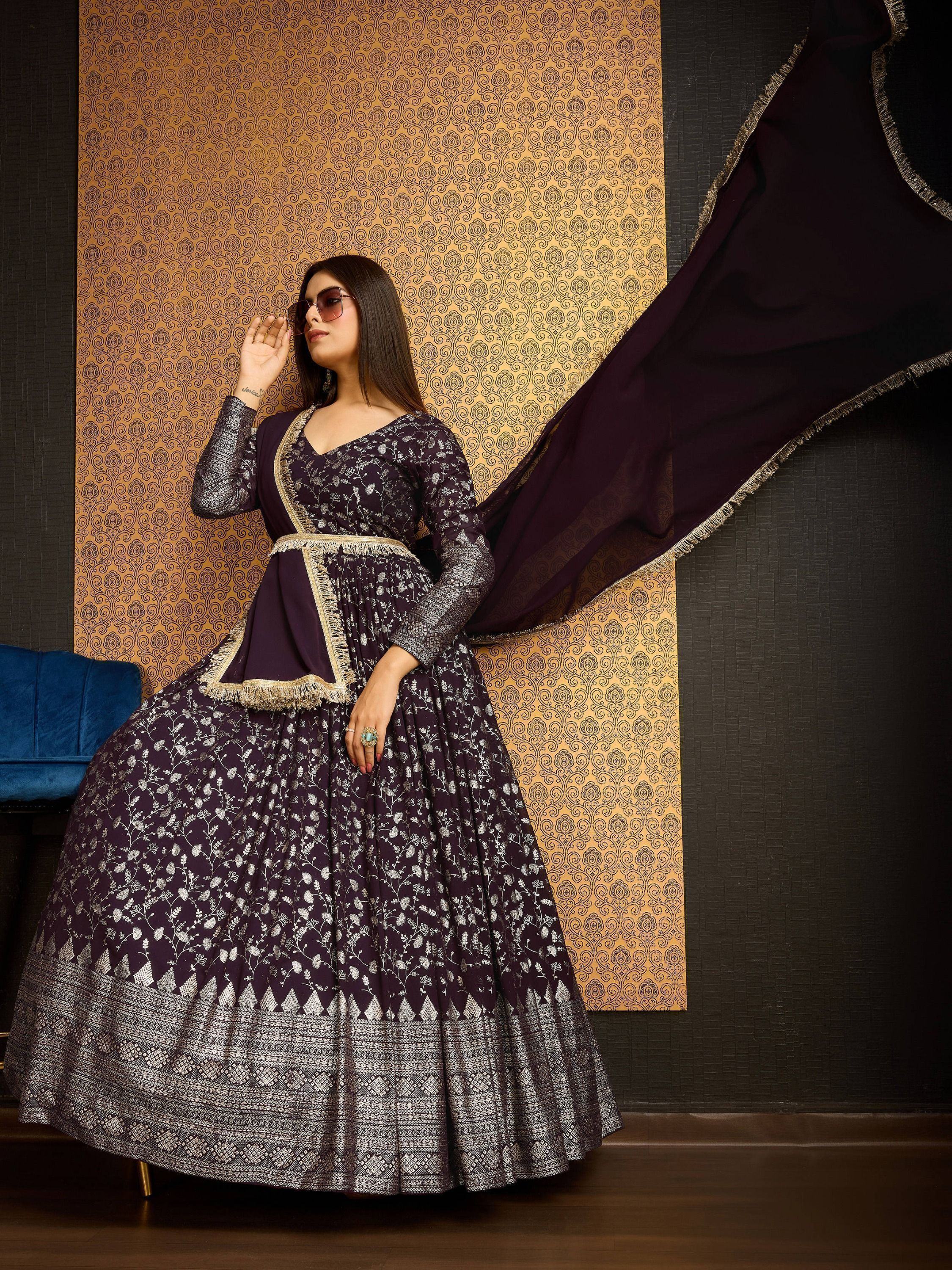 Woman in purple embroidered Anarkali gown with dupatta, posing against gold patterned wall