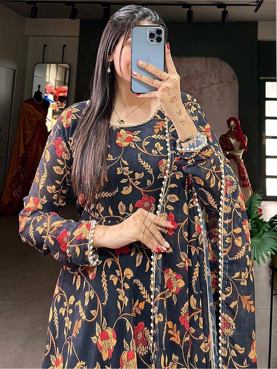 Woman in black floral ethnic gown with pearl trim, henna hands, taking mirror selfie in boutique