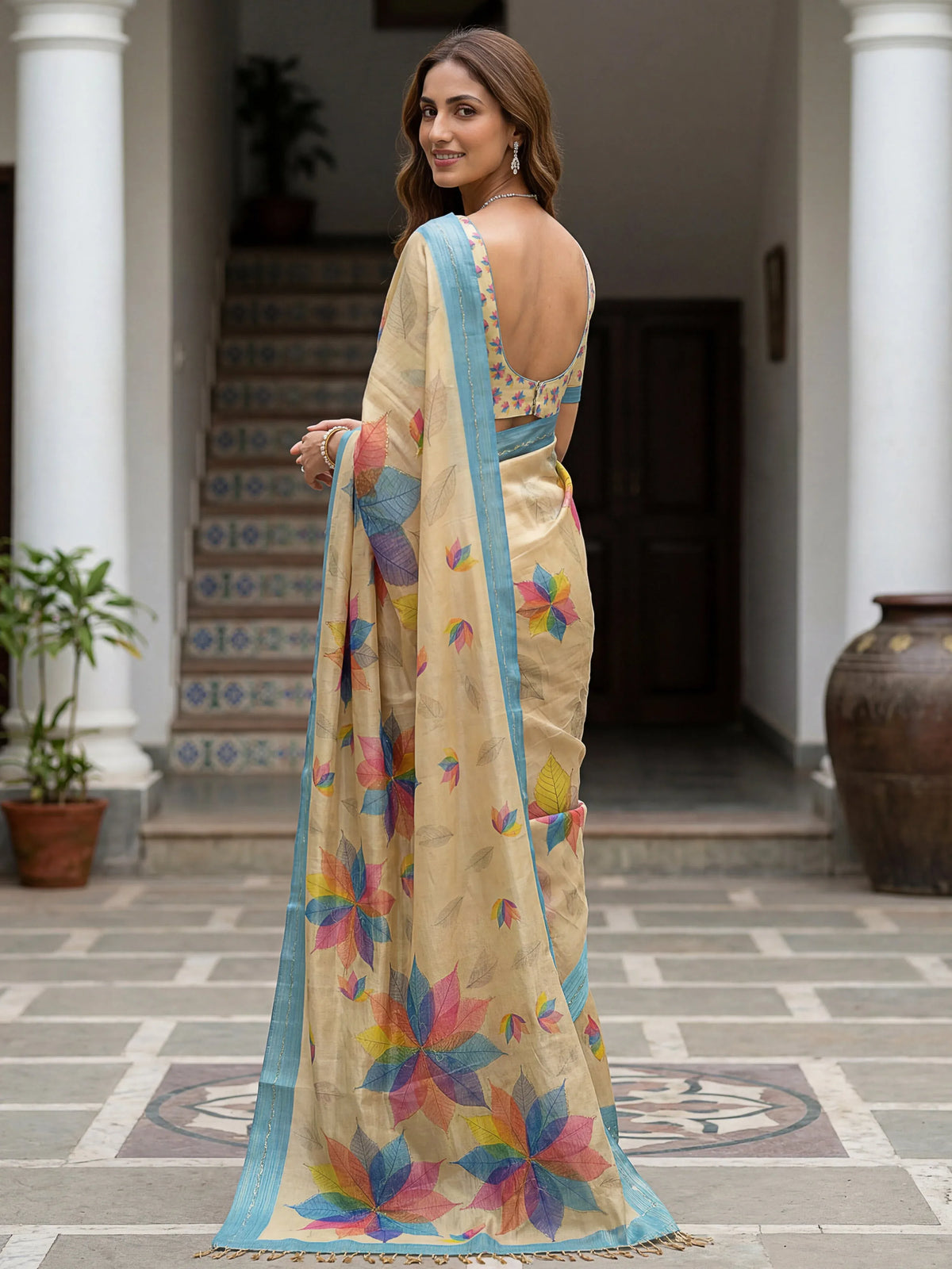 Woman wearing a beige designer saree with colorful leaf prints and a blue border