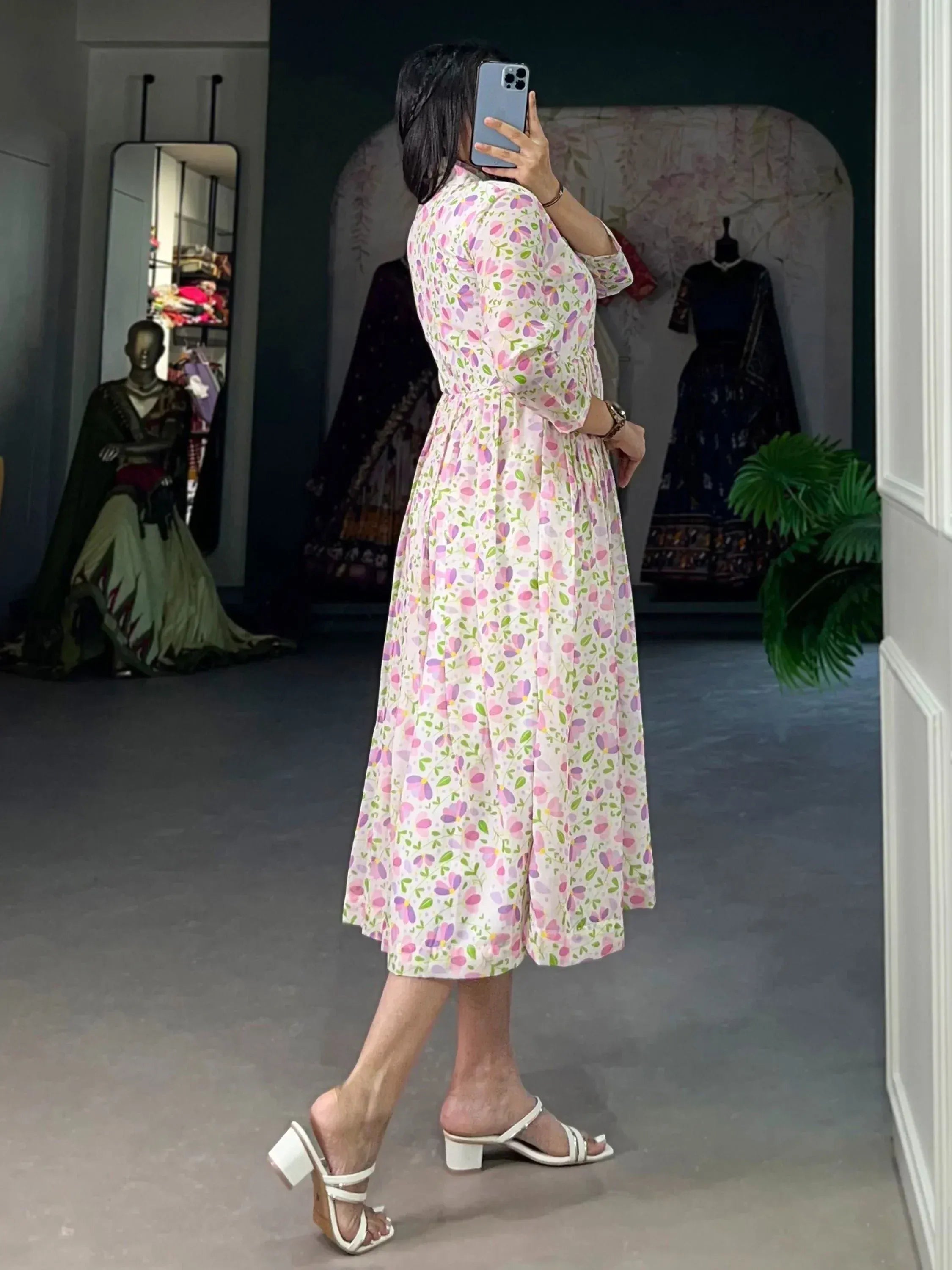 Woman in floral print ethnic gown with white heels, mirror selfie in boutique