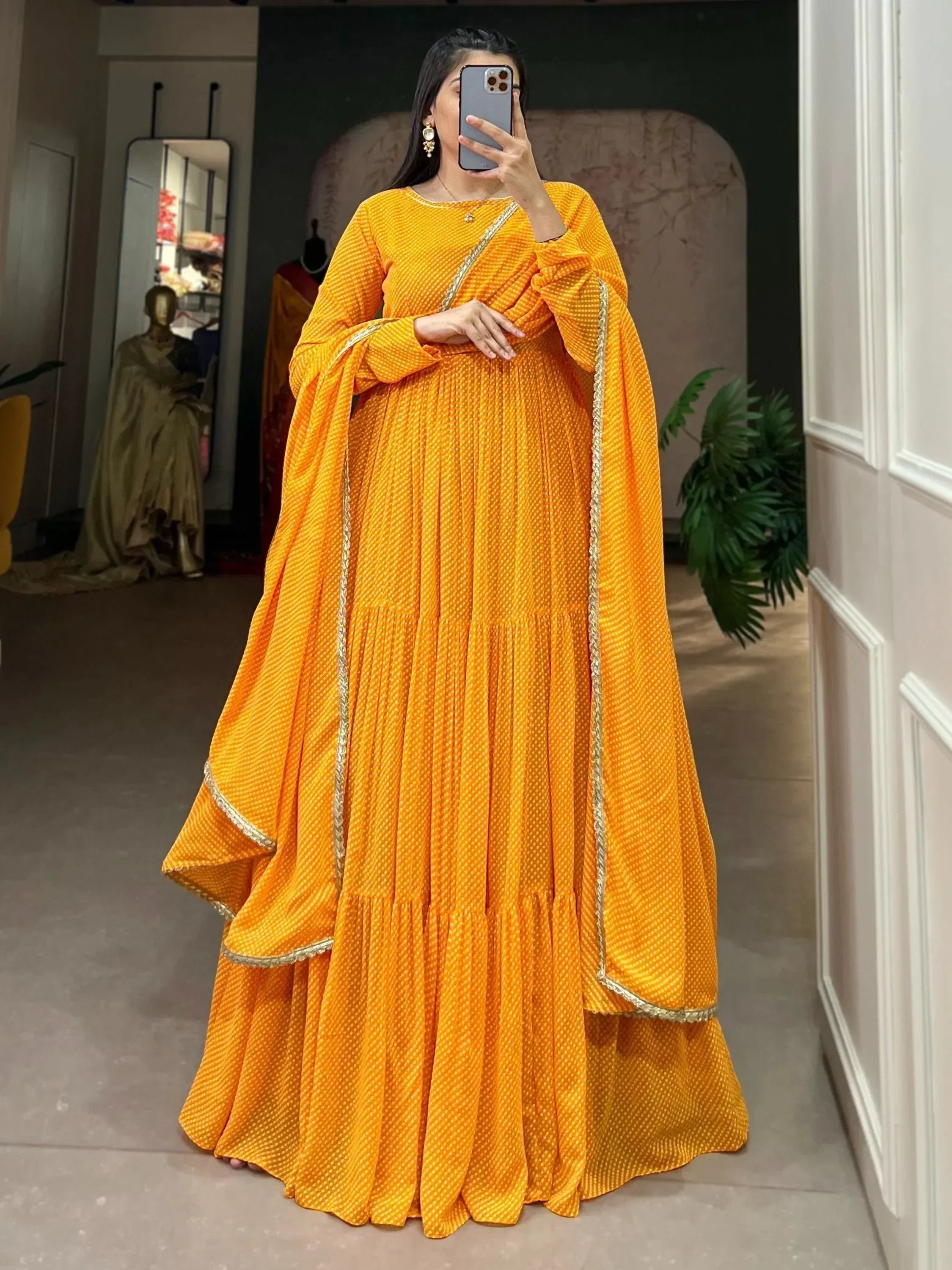 Vibrant orange ethnic gown with gold trim, pleated design, and long sleeves for Indian occasions
