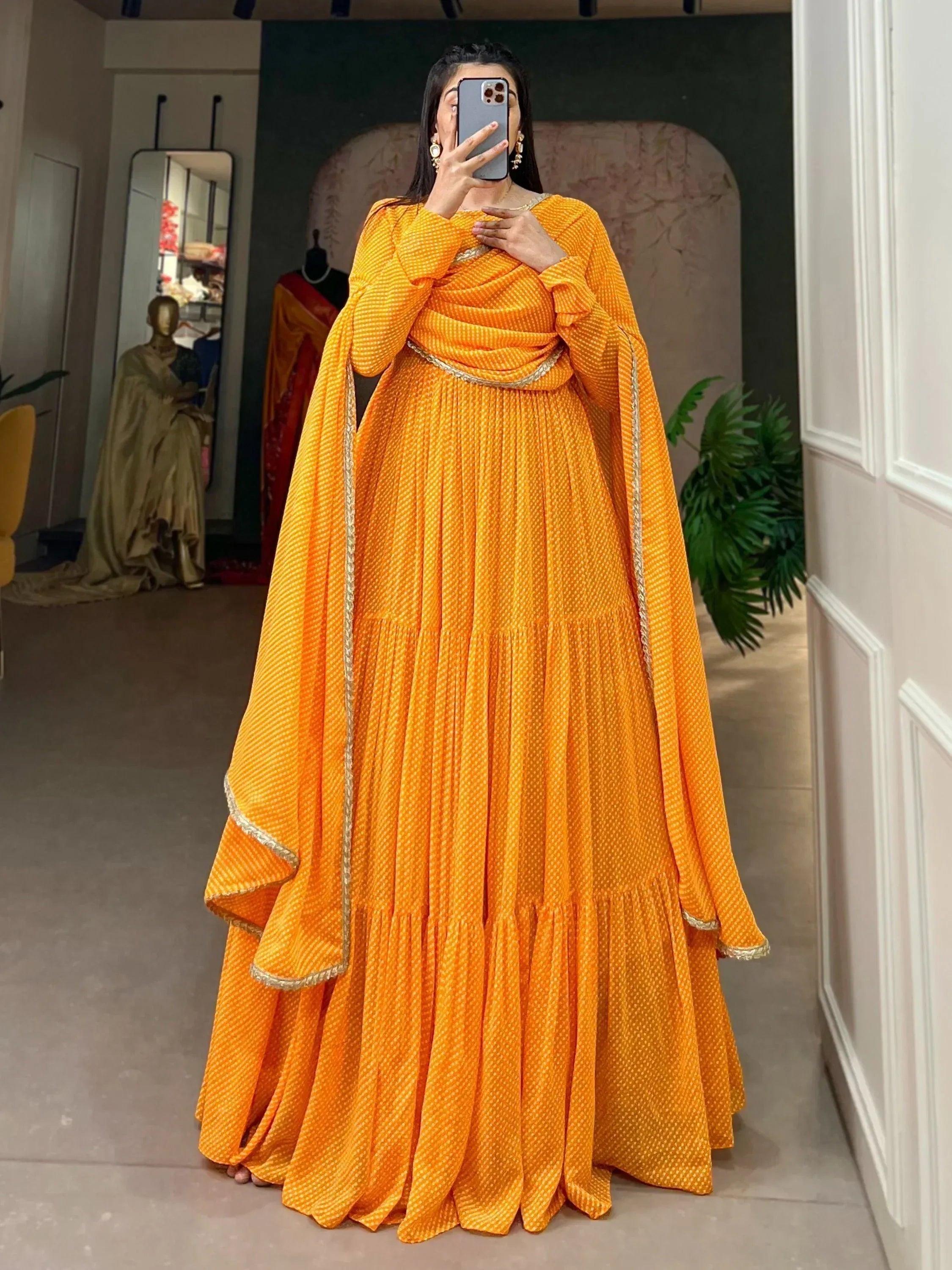 Vibrant orange ethnic gown with gold trim, pleated design, and long sleeves for festive occasions