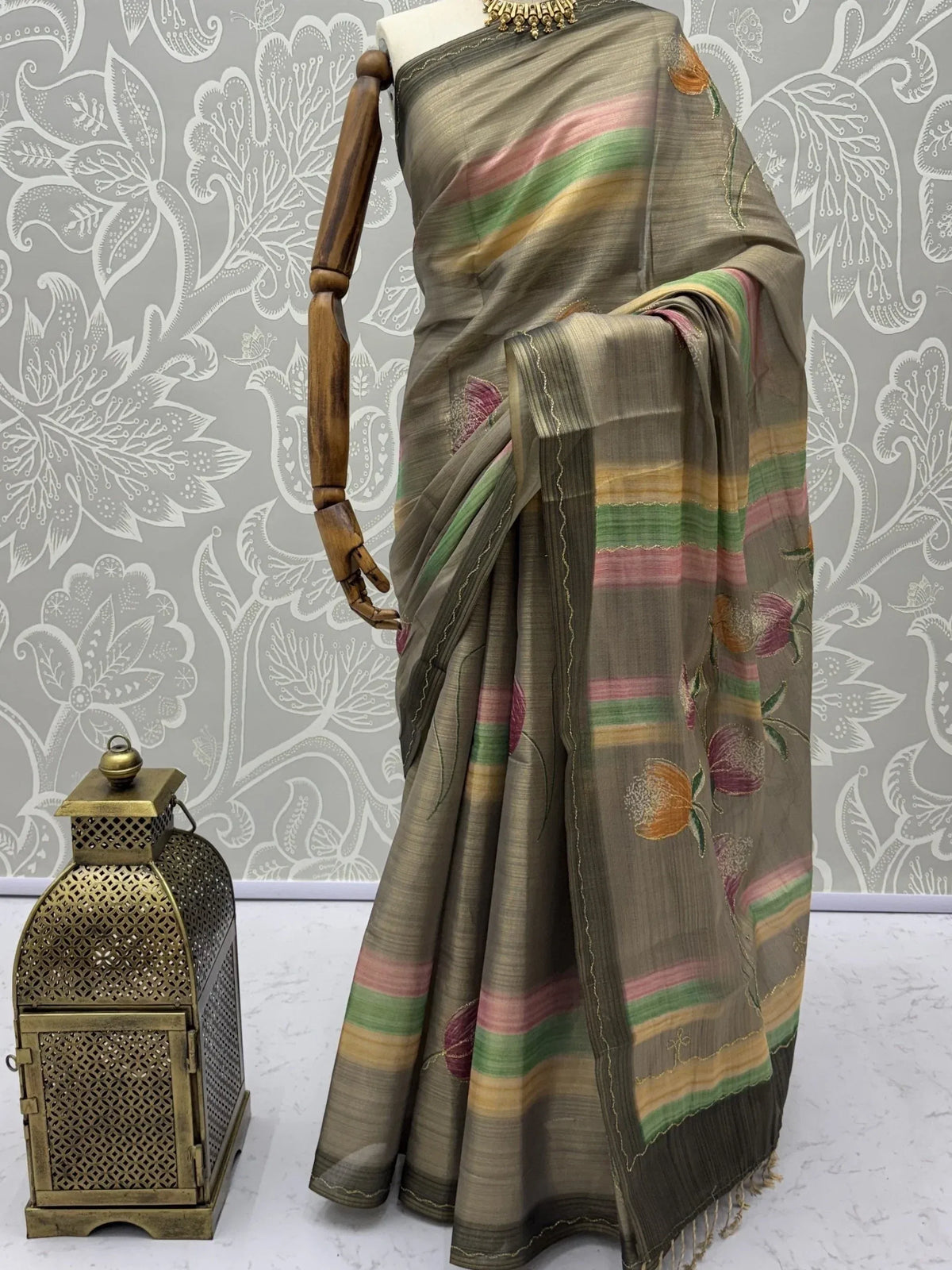 Olive green designer saree with colorful stripes and floral embroidery on a mannequin