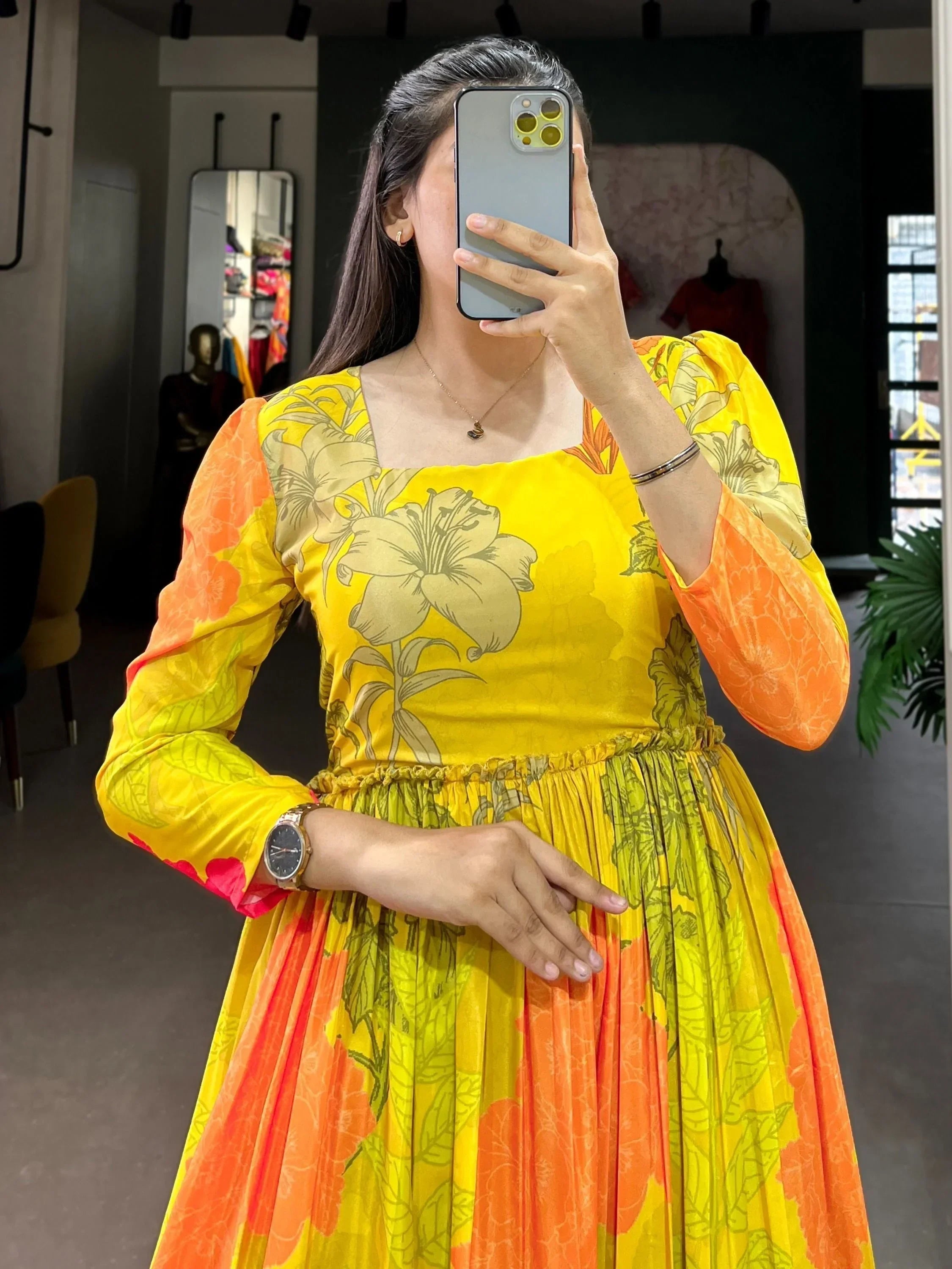 Woman wearing yellow floral printed ethnic gown with long sleeves, taking mirror selfie
