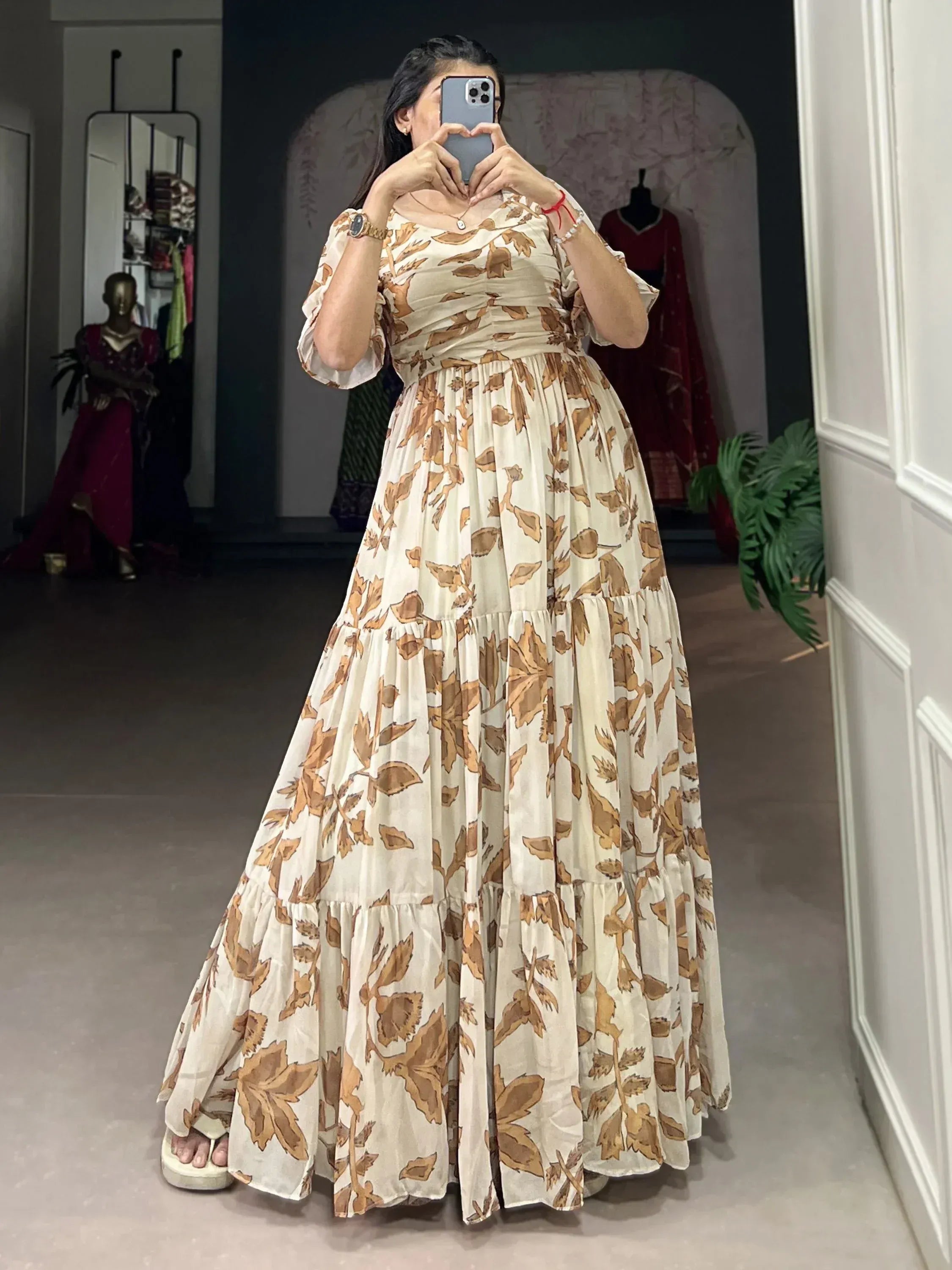 Woman wearing a cream and brown floral ethnic gown, taking a mirror selfie indoors