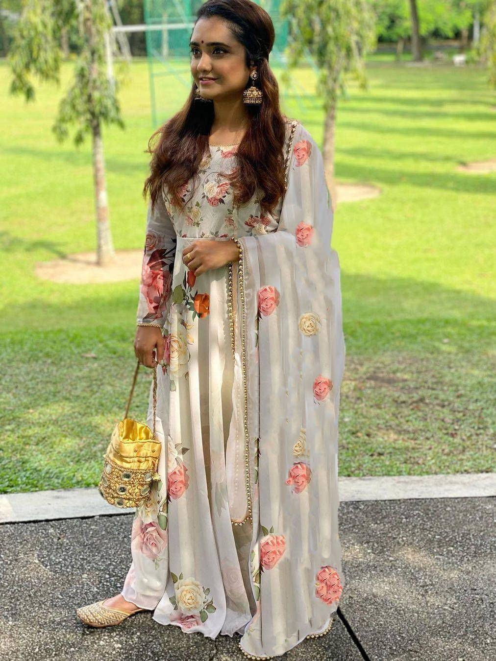 Woman in floral print Indian ethnic gown with dupatta, gold embellishments, and matching potli bag