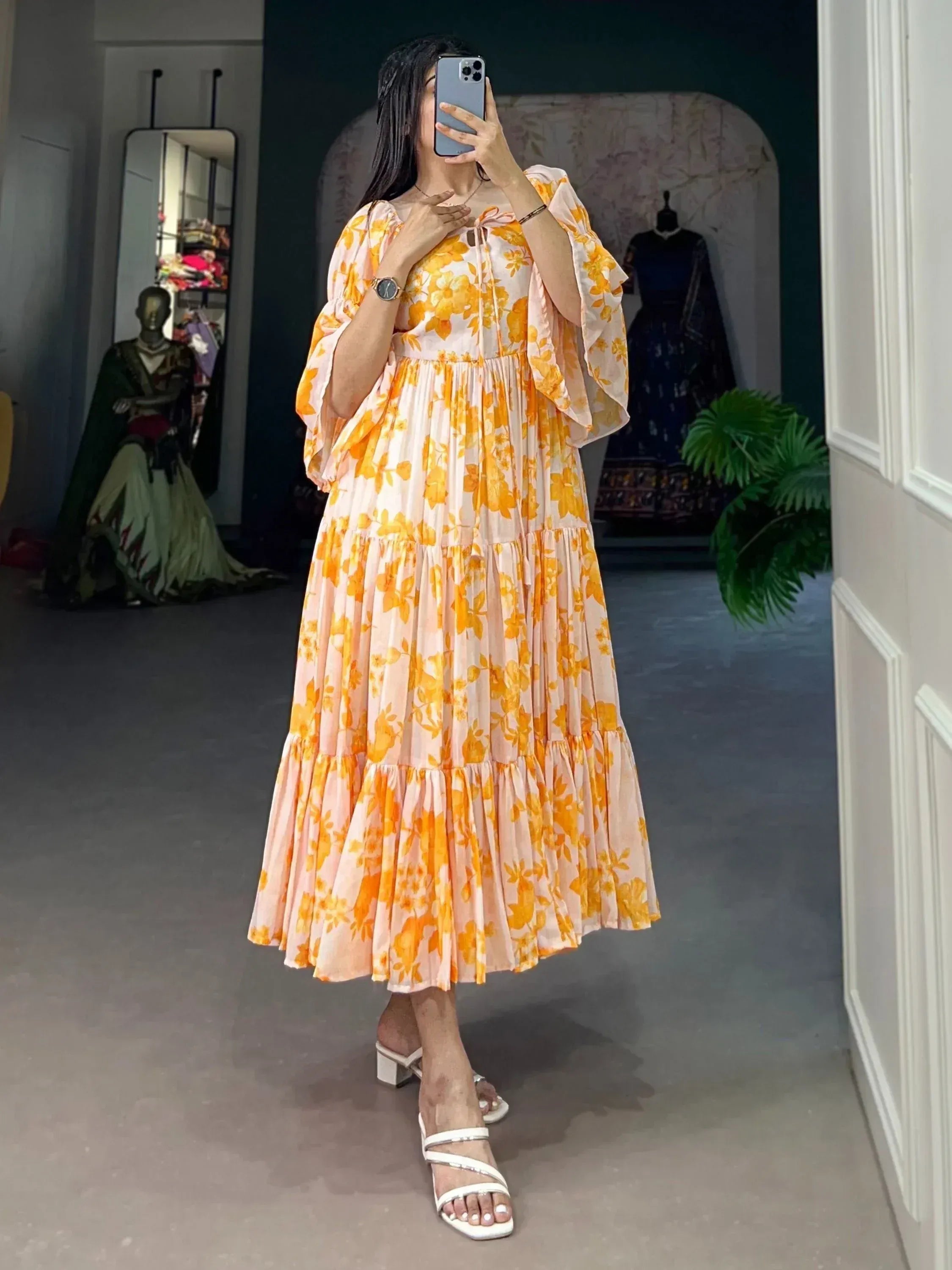 Woman wearing a yellow floral print maxi dress with flared sleeves, taking a mirror selfie indoors