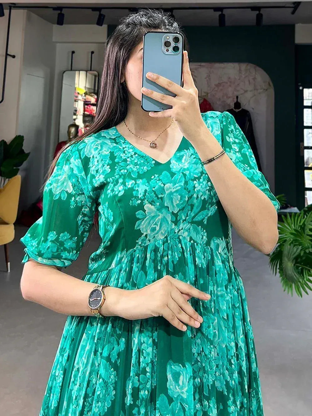 Woman in green floral ethnic gown with puff sleeves, V-neck, pleated skirt, taking mirror selfie in boutique