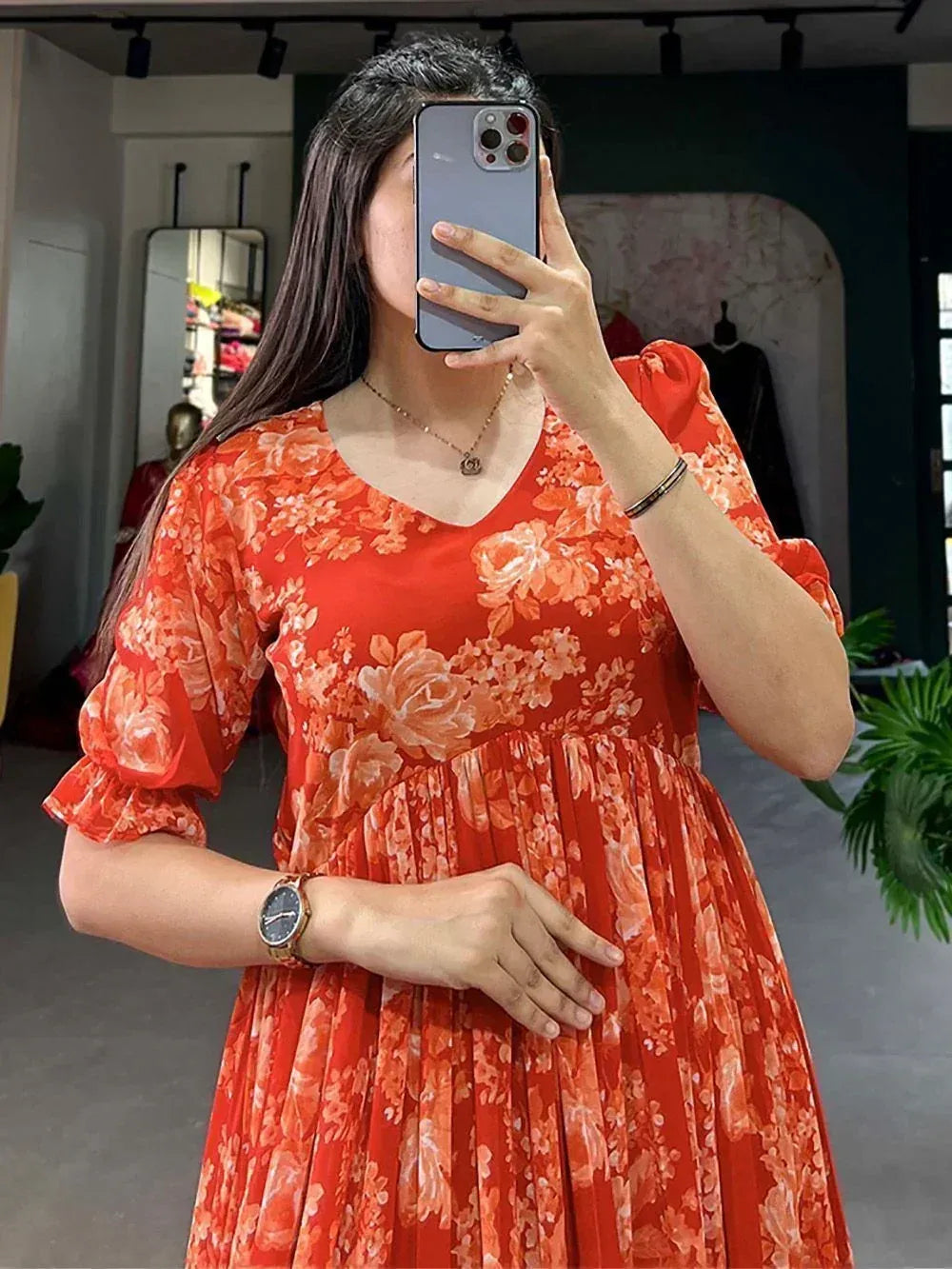 Woman in orange floral ethnic gown with puff sleeves, taking mirror selfie in boutique