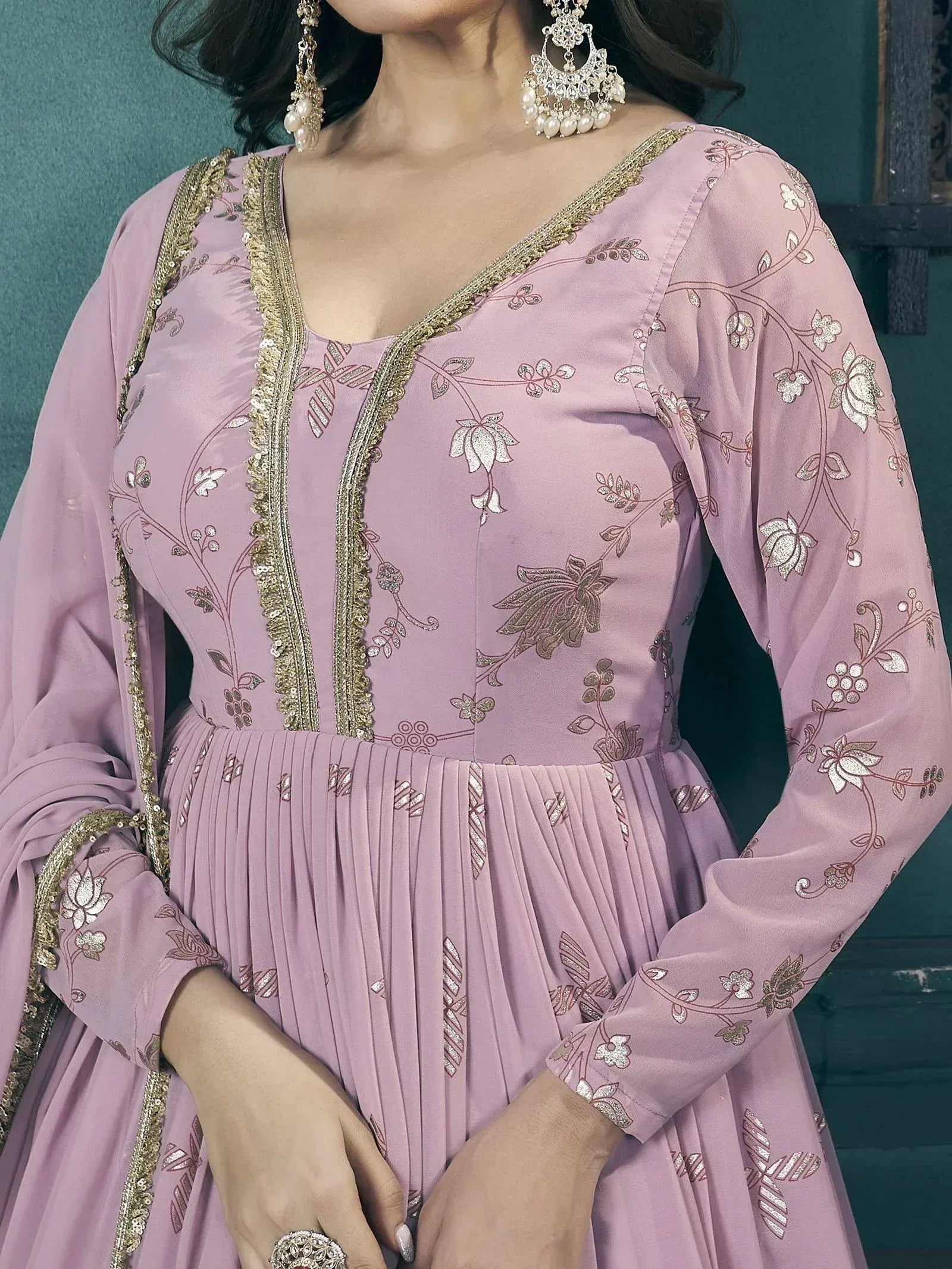 Pink floral embroidered ethnic gown with gold trim and pleated skirt, paired with statement earrings.