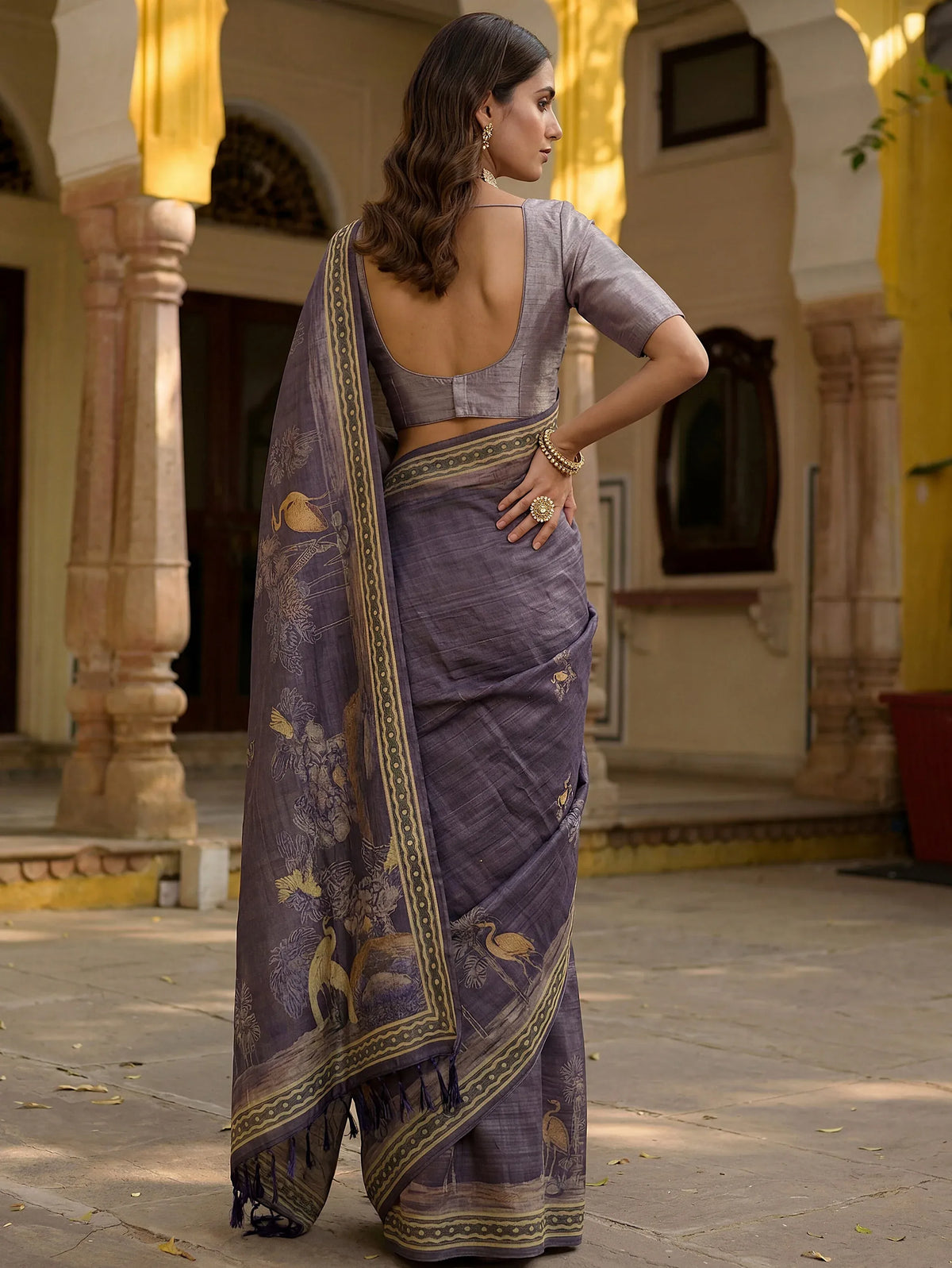 Woman wearing a purple designer saree with gold embroidery in a traditional courtyard.