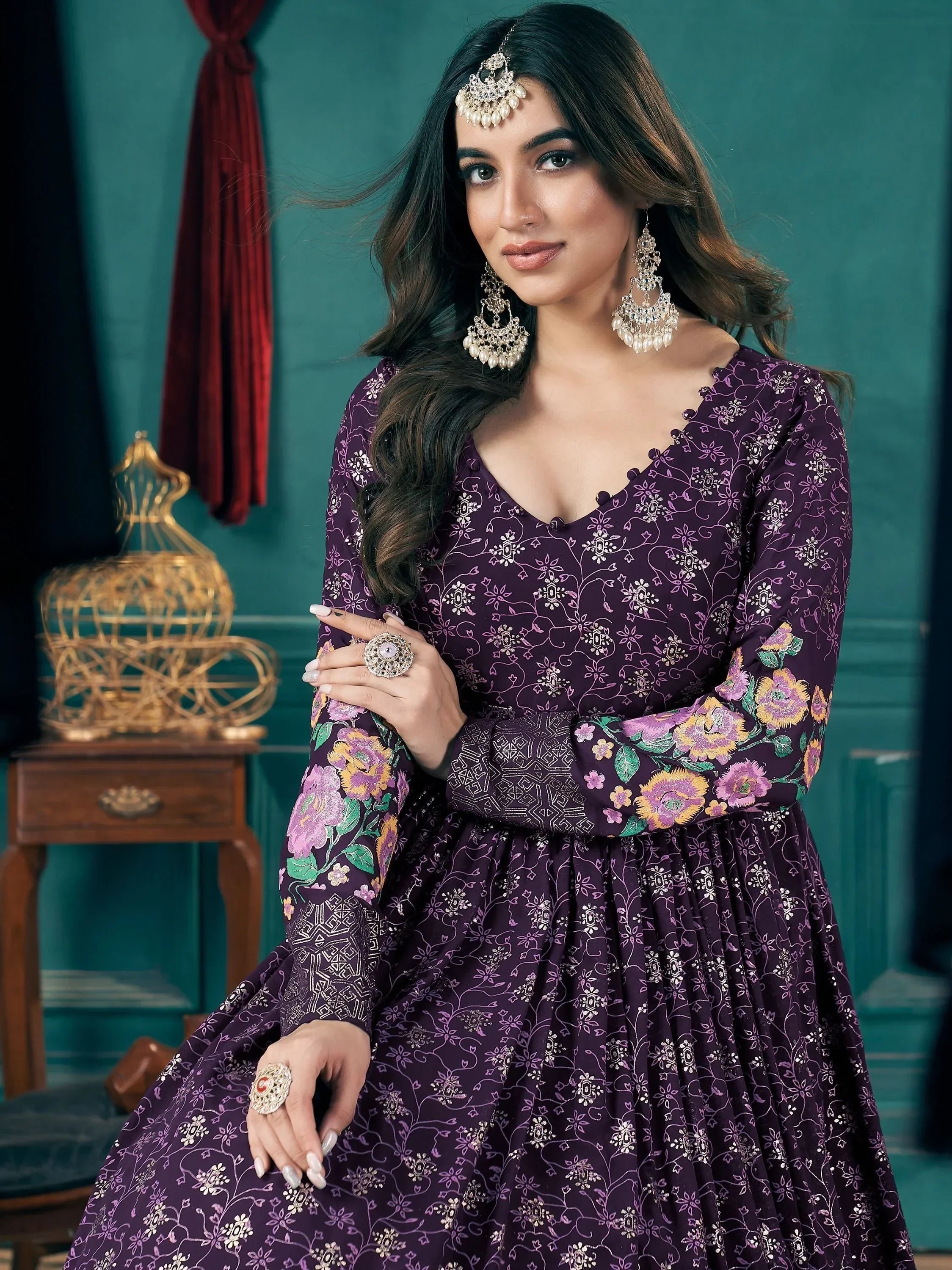 Woman in purple floral embroidered ethnic gown with long sleeves, statement jewelry, elegant indoor setting