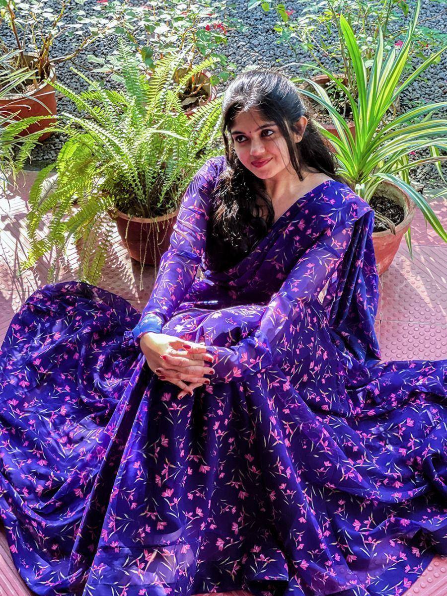 Woman in purple floral ethnic gown, sitting outdoors with potted plants, perfect for Indian occasions.