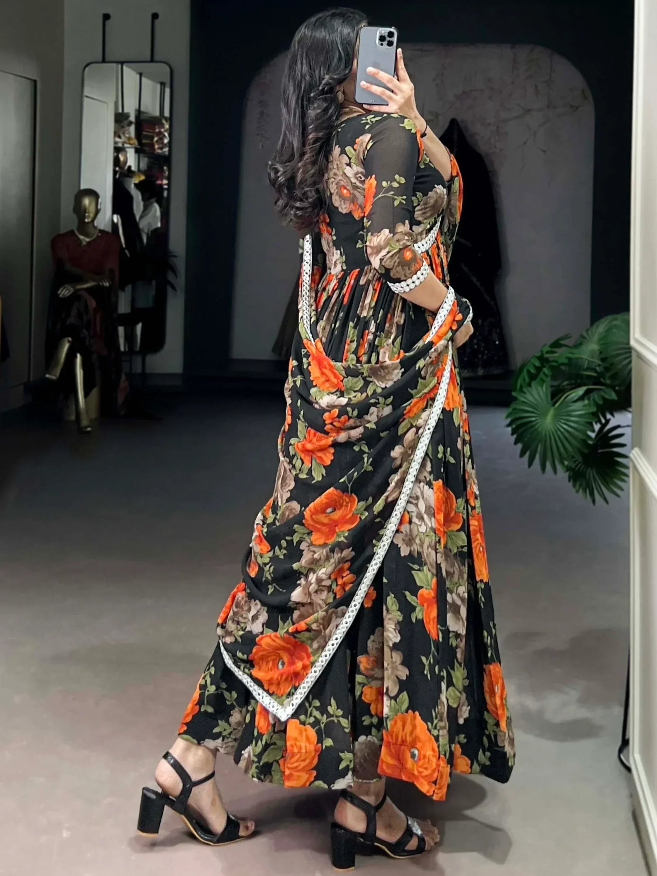 Black floral ethnic gown with orange roses, white trim, and pleated design, styled with black heels in boutique setting