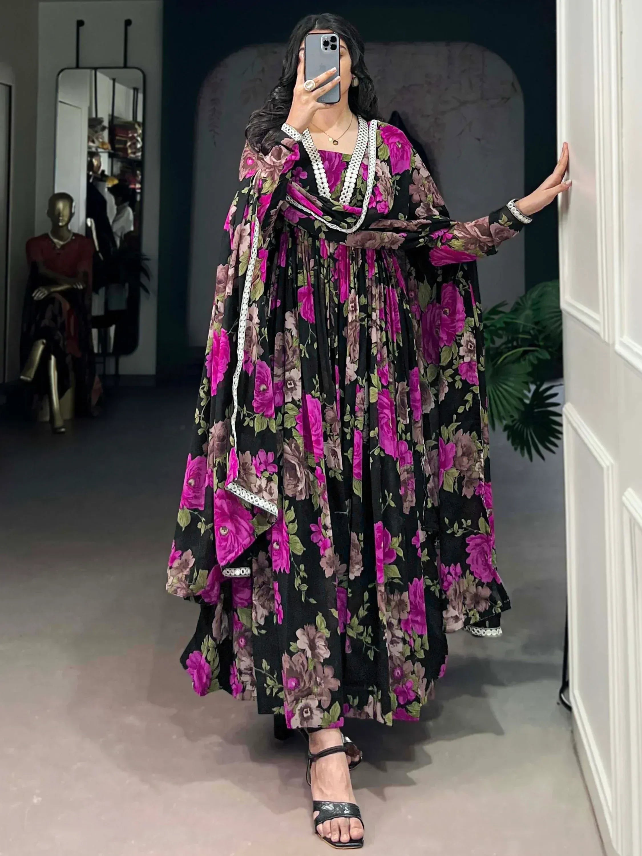 Woman in black floral ethnic gown with white trim, taking mirror selfie in boutique