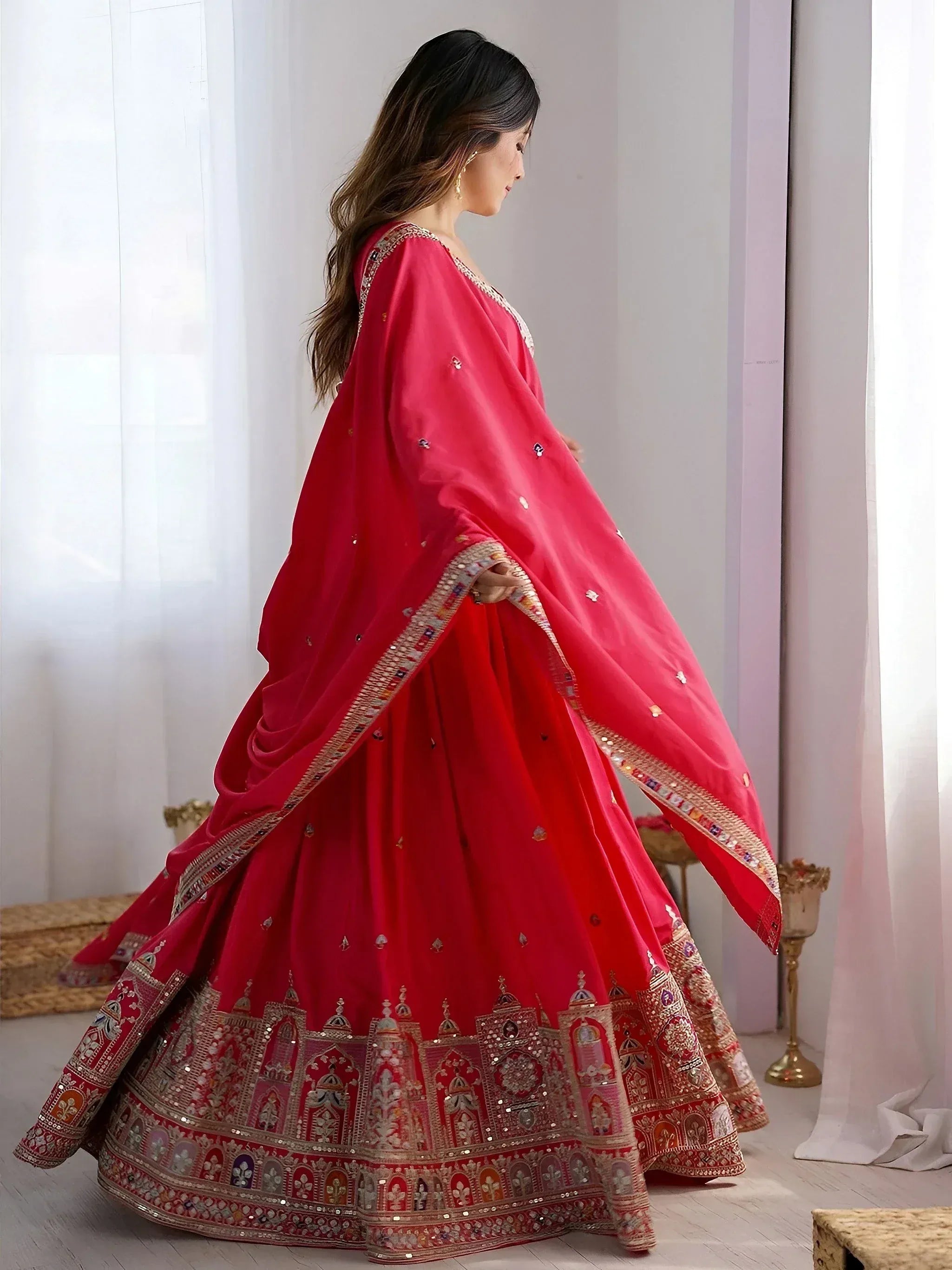 Woman in red designer lehenga choli with intricate embroidery and mirror work, perfect for Indian weddings or festive occasions.