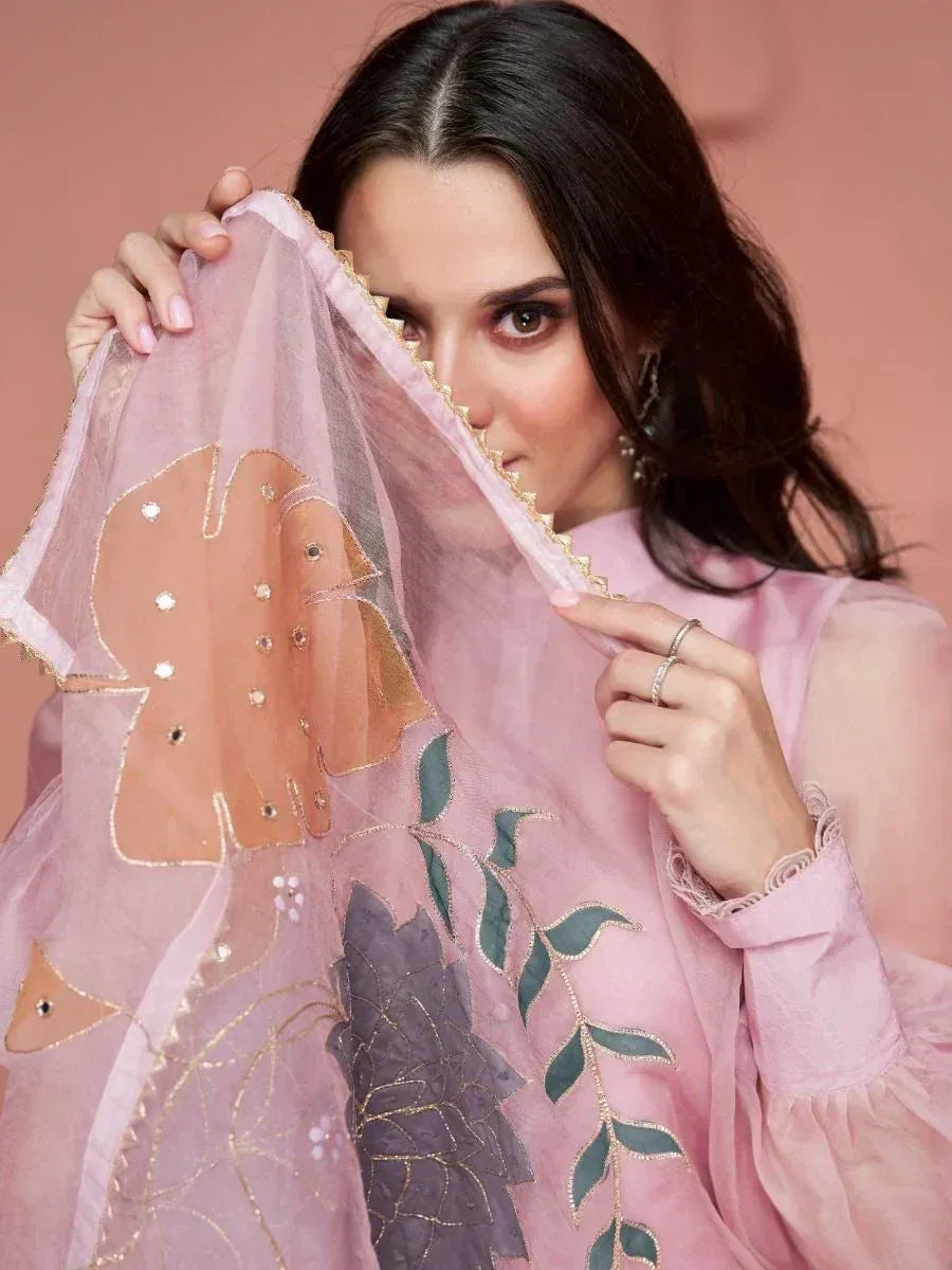 Woman in sheer pink saree with floral embroidery, holding dupatta near face
