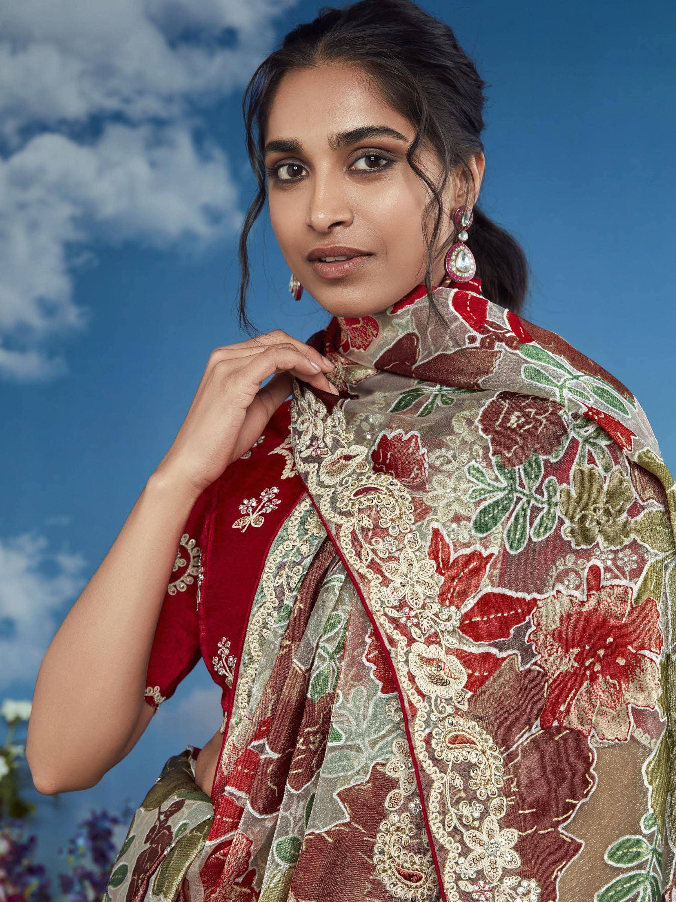 Woman in red floral embroidered saree with gold detailing, styled with statement earrings against blue sky