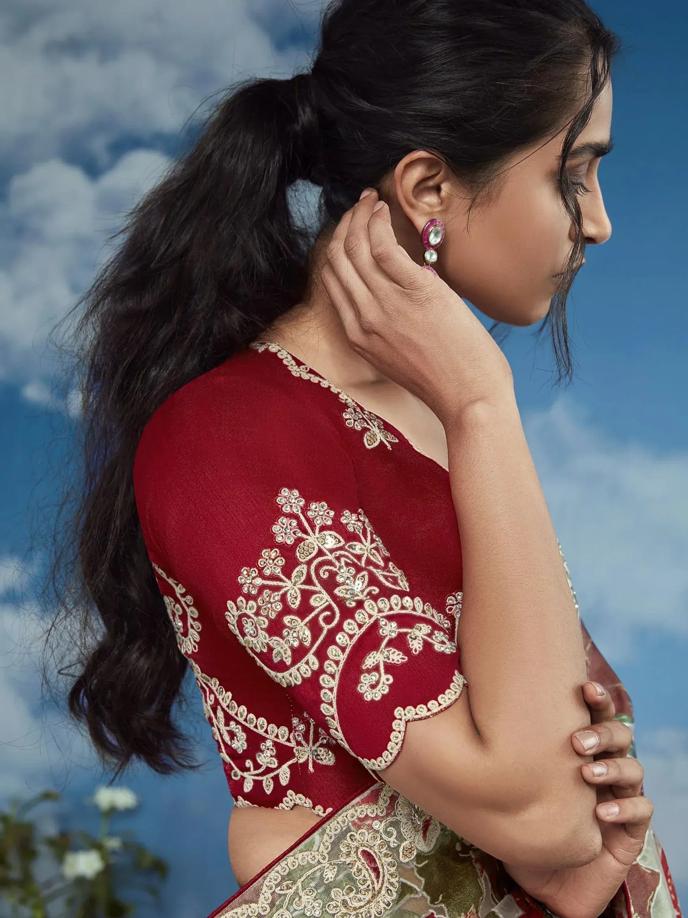 Woman in red embroidered saree blouse with gold detailing, sky background