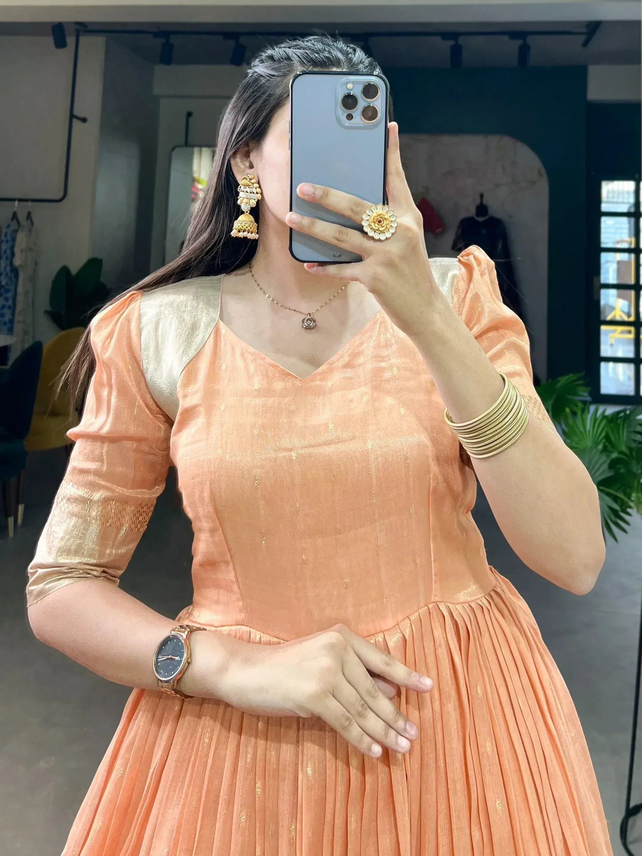 Peach ethnic gown with gold accents, puff sleeves, and pleated skirt, styled with jhumka earrings and bangles.
