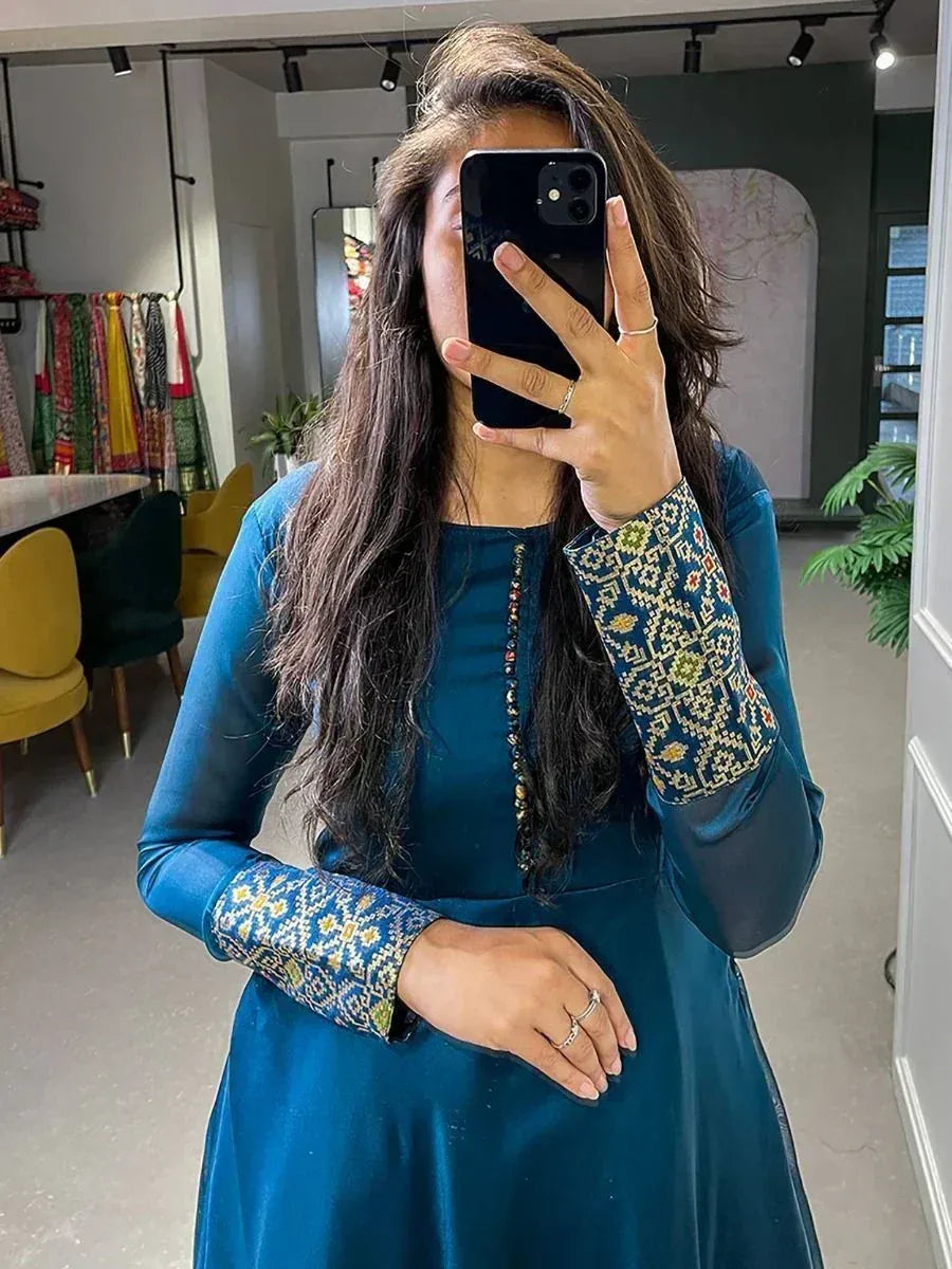 Woman in teal ethnic gown with embroidered sleeves, taking mirror selfie in boutique