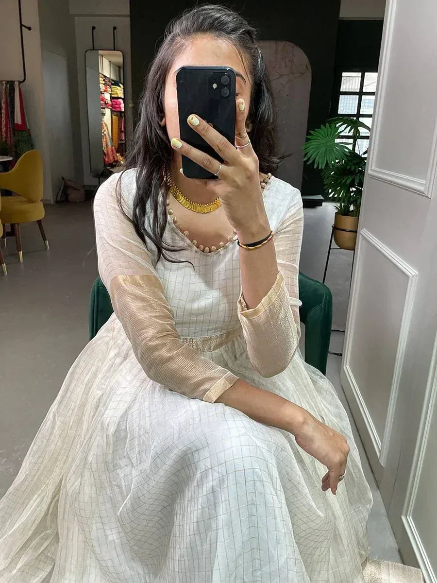 Woman in white checkered ethnic gown with gold jewelry, taking mirror selfie in boutique