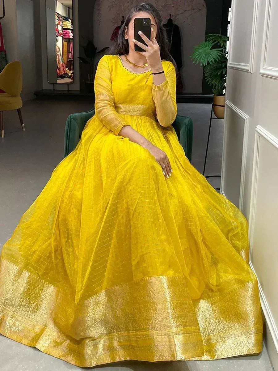 Woman in a yellow silk ethnic gown with gold border sitting indoors, taking a mirror selfie.