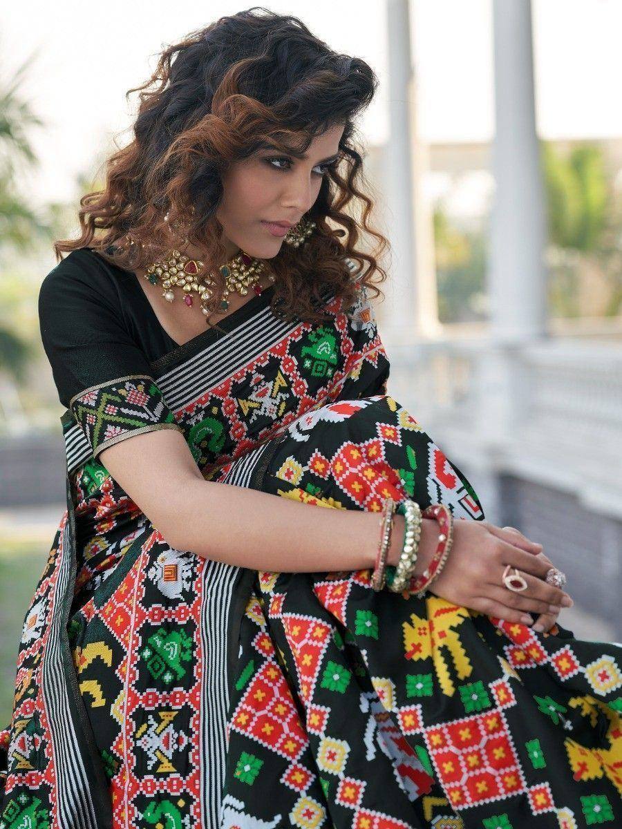 Woman in vibrant black ethnic saree with colorful geometric print, paired with gold jewelry and bangles