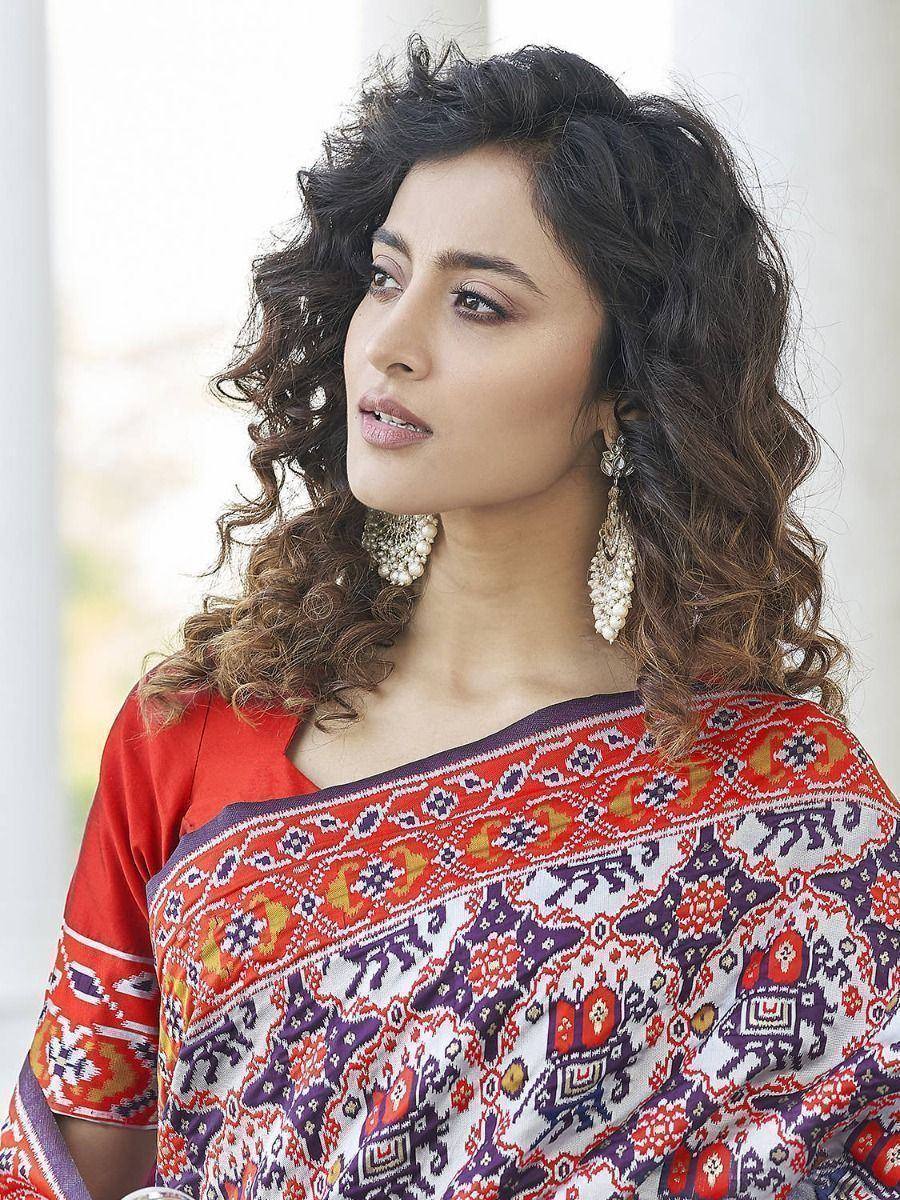 Woman in vibrant red and purple ethnic saree with elephant print, styled with curly hair and jhumka earrings